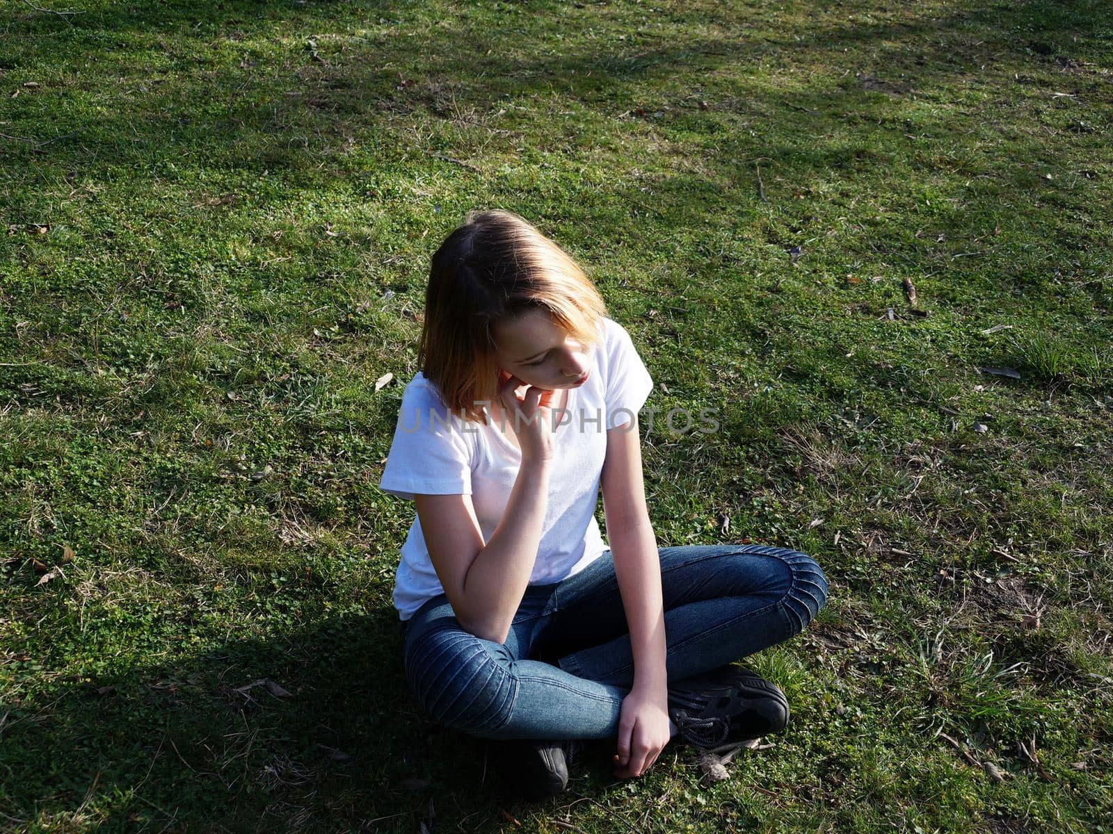 sad pensive teenage girl sitting on the grass in the park by Annado