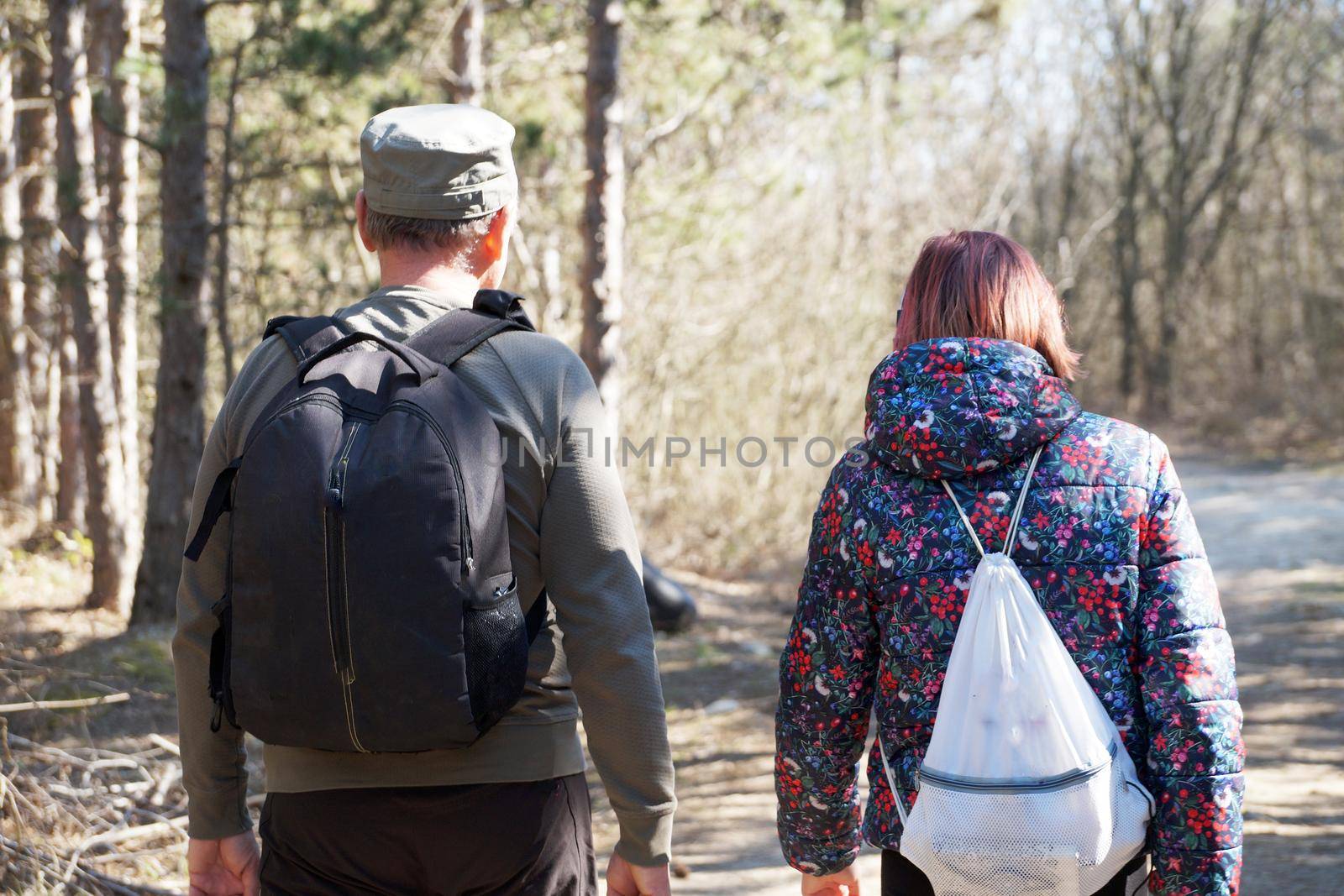 a man and a teenage girl are walking with backpacks along a forest road on a sunny day, back view