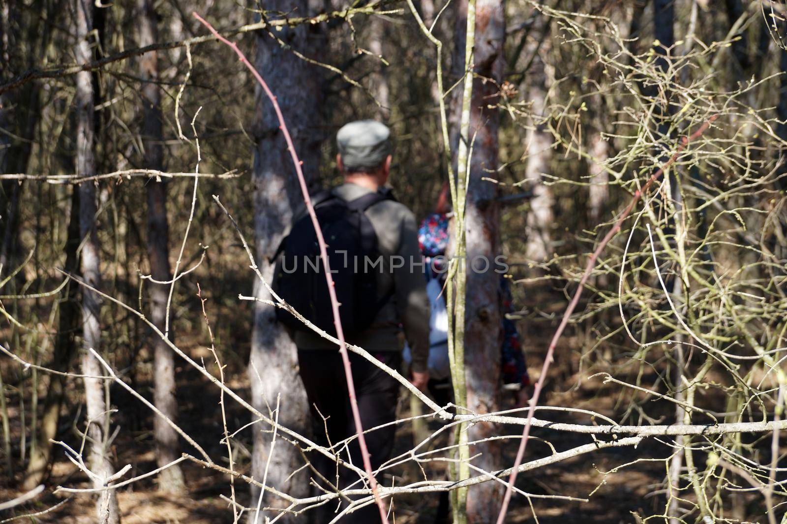 a man and a girl with backpacks make their way through a dense forest.