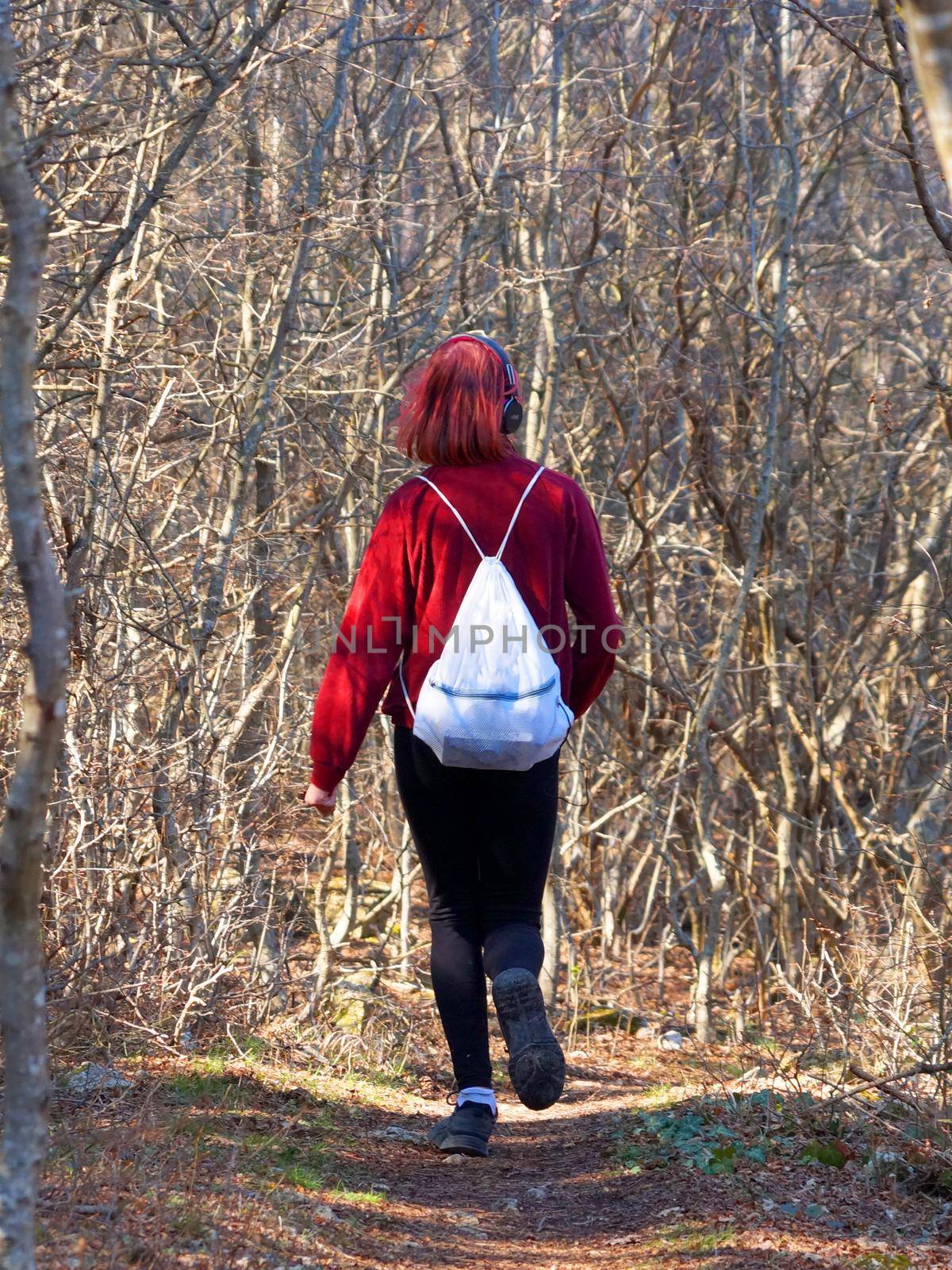 teenage girl in headphones runs along a forest trail with a backpack, back view