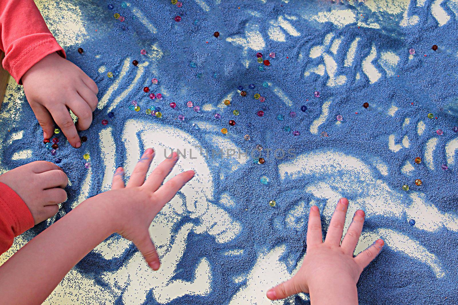 childrens hands touching blue sand on white table sand therapy, development of fine motor skills by Annado