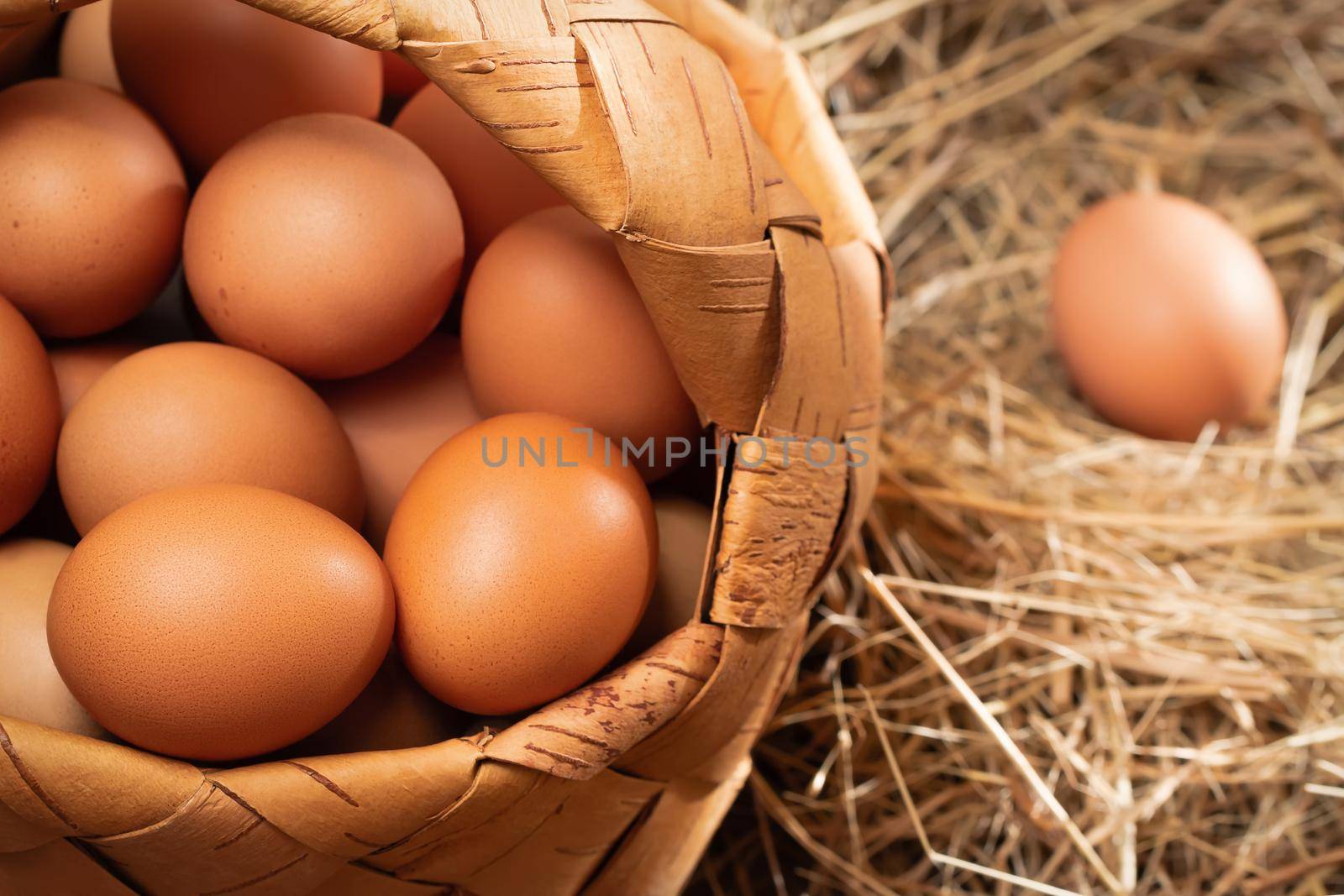 Fresh brown chicken eggs in a basket and in a nest from hay in a barn.