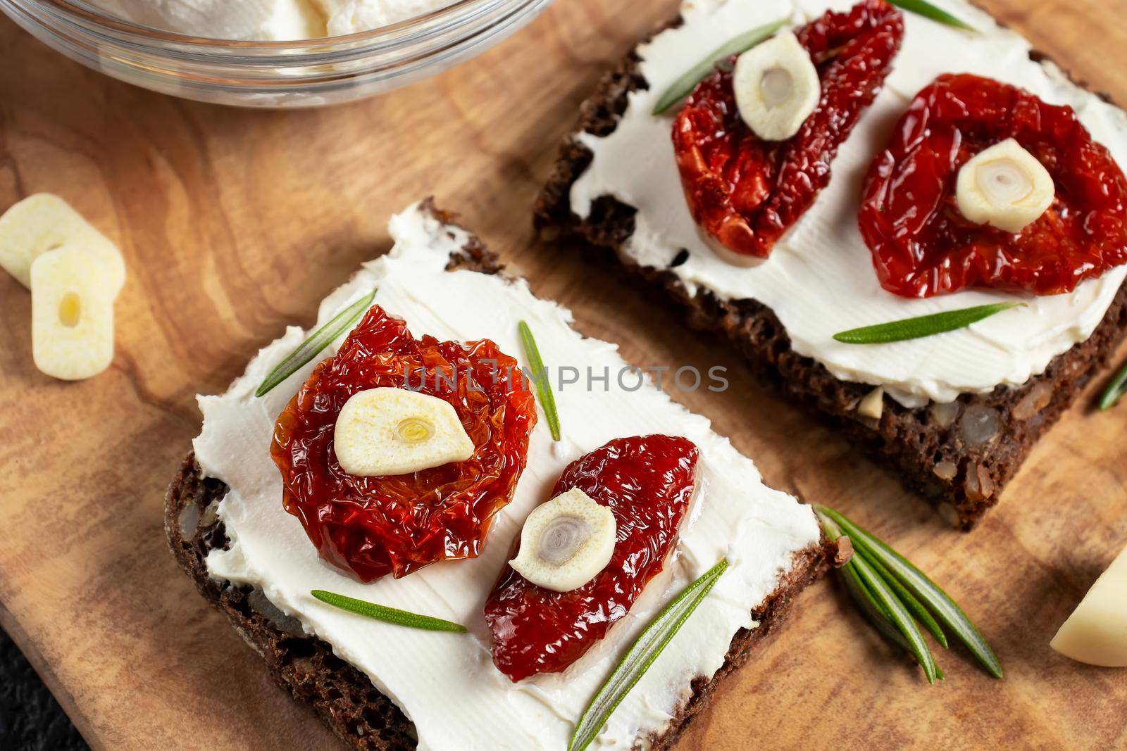 Homemade multigrain bread sandwiches with cream cheese and sun-dried tomatoes on a wooden platter, close-up. Healthy eating concept.