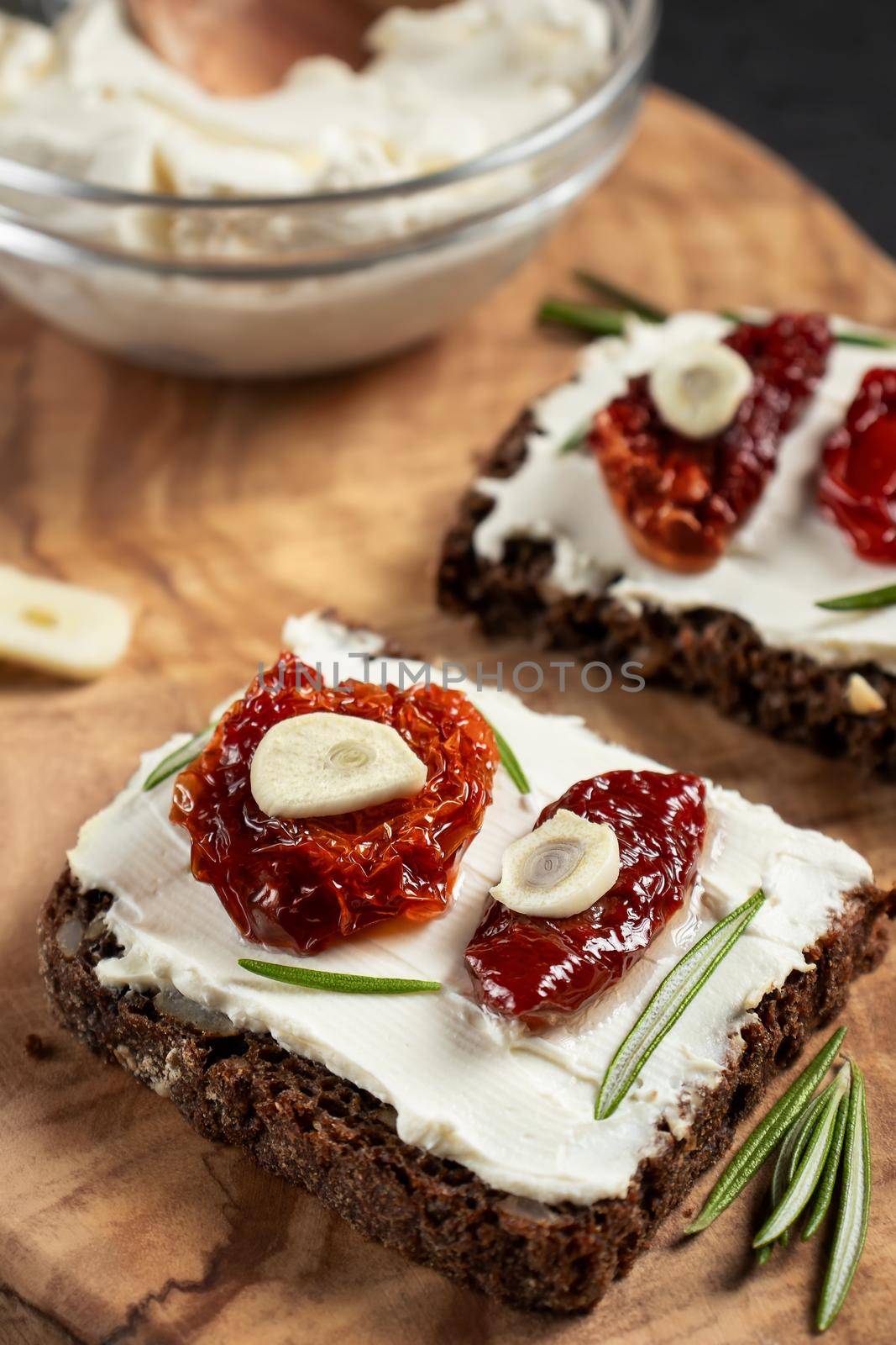 Homemade multigrain bread sandwiches with cream cheese and sun-dried tomatoes on a wooden platter. Healthy eating concept. Vertical image by galsand