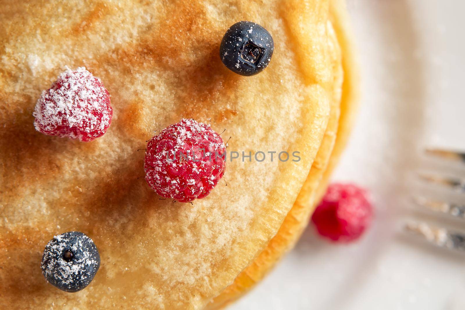 Stack of pancakes with fresh berries on a white plate close up, top view by galsand