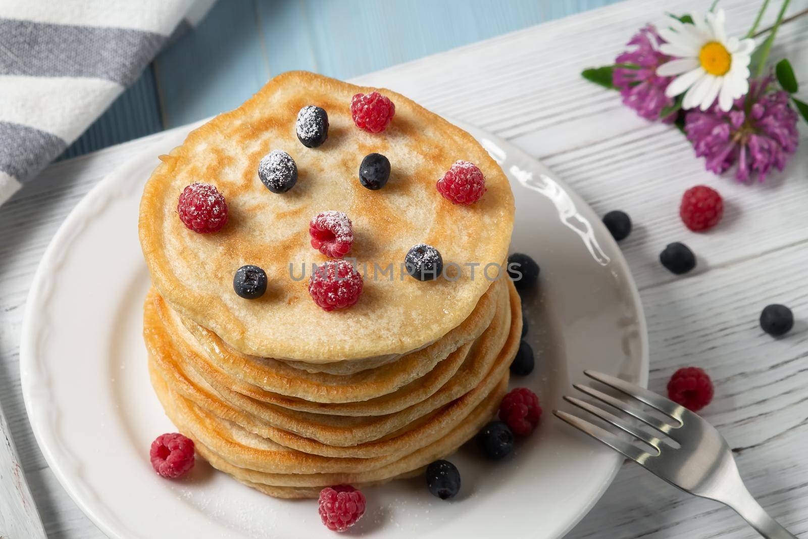 Stack of pancakes with fresh berries on a white plate on the table.