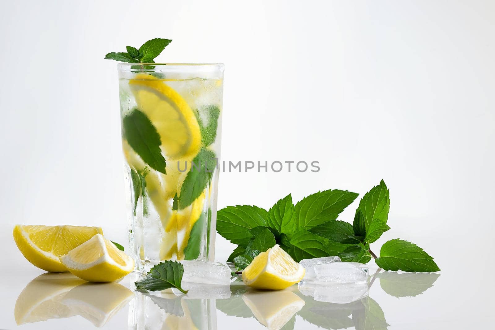 Fresh homemade cocktail in a tall glass with lemon, mint and ice on a white background, copy space by galsand