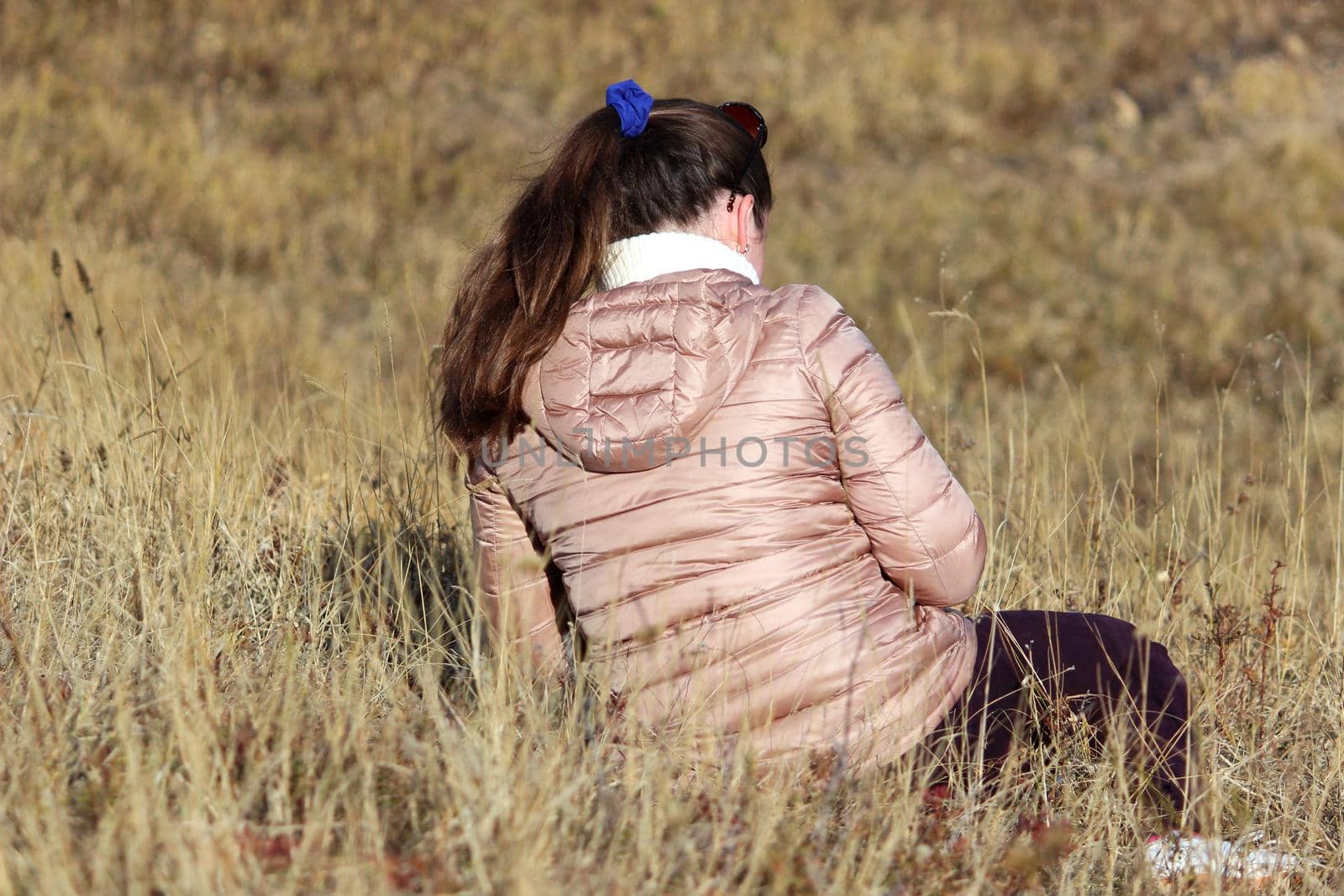 The girl sits alone in a field in the fall on dry grass. by Olga26