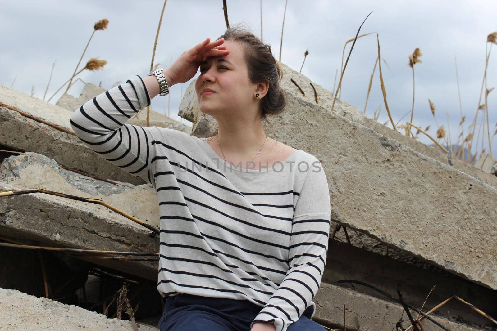 A portrait of an outdoor girl sits in a field on large concrete slabs. High quality photo