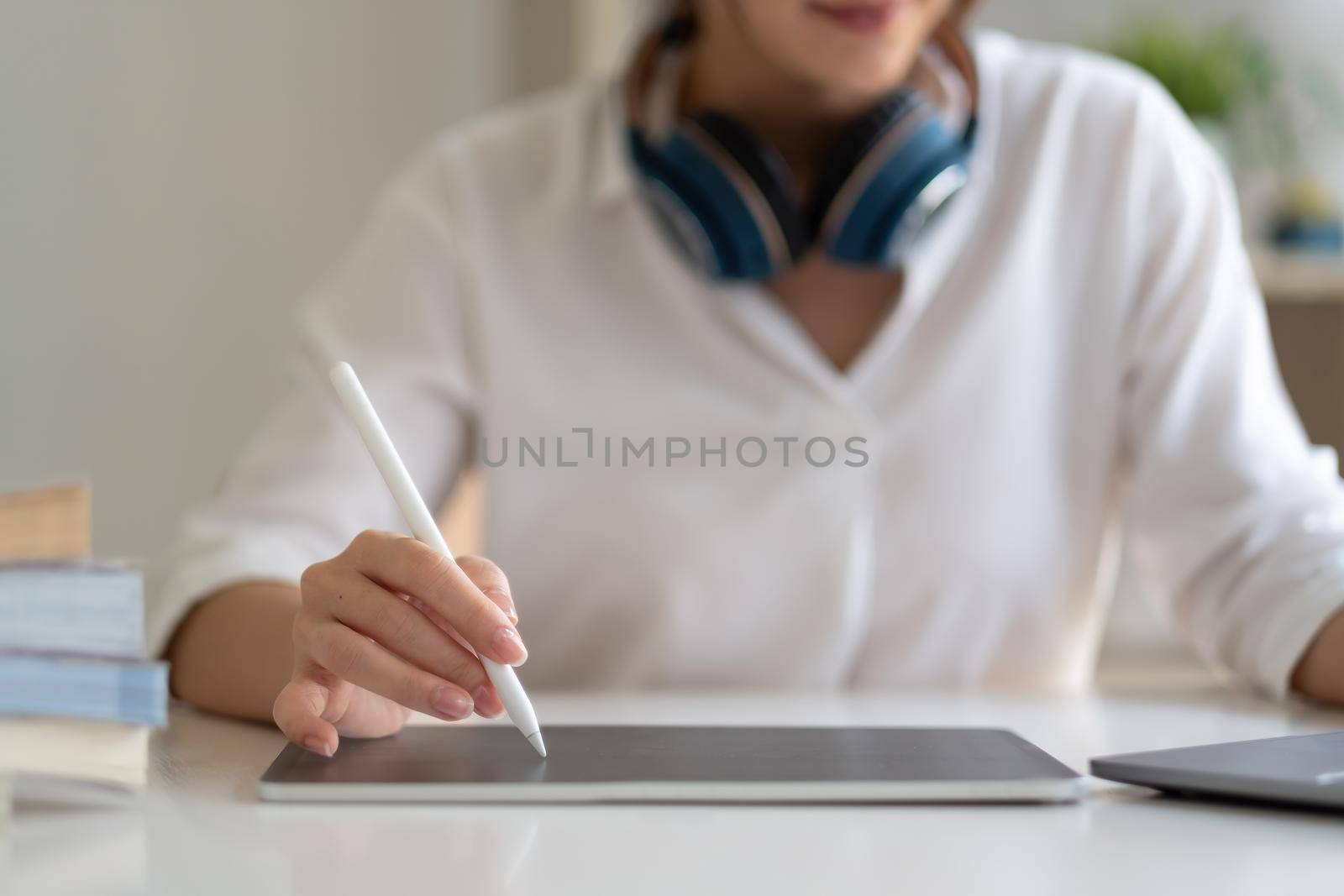 Close up of female worker working from home with digital tablet, laptop and headphone in home office room