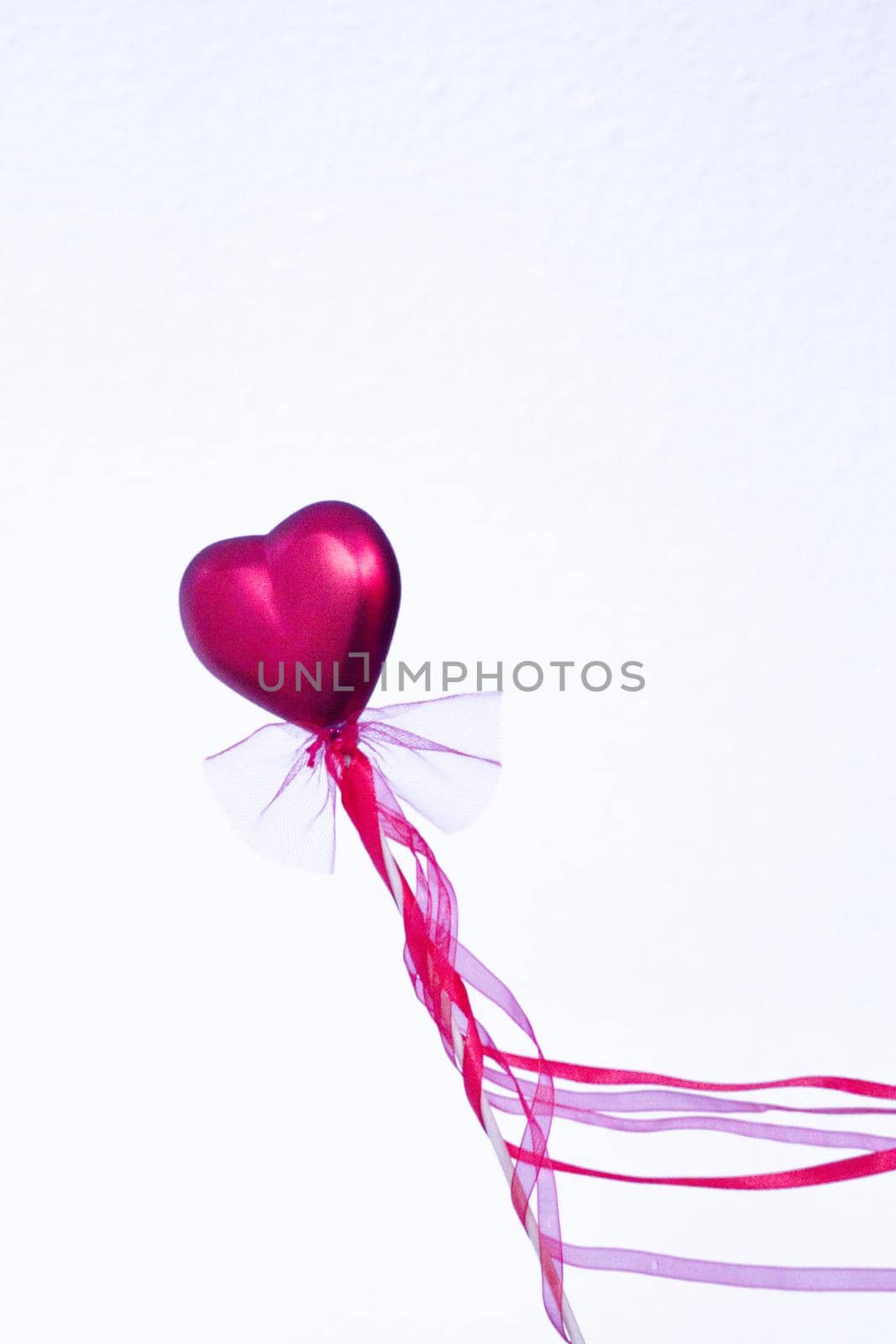 Red heart attached to a stick with a bow hanging. Copy space