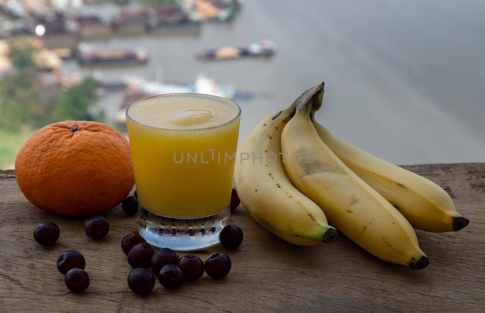 Healthy ripe Yellow Mango Smoothie in Glass and Banana, Orange and Grape rustic old wooden table with river view. Tropical fruit concept. Selective focus.