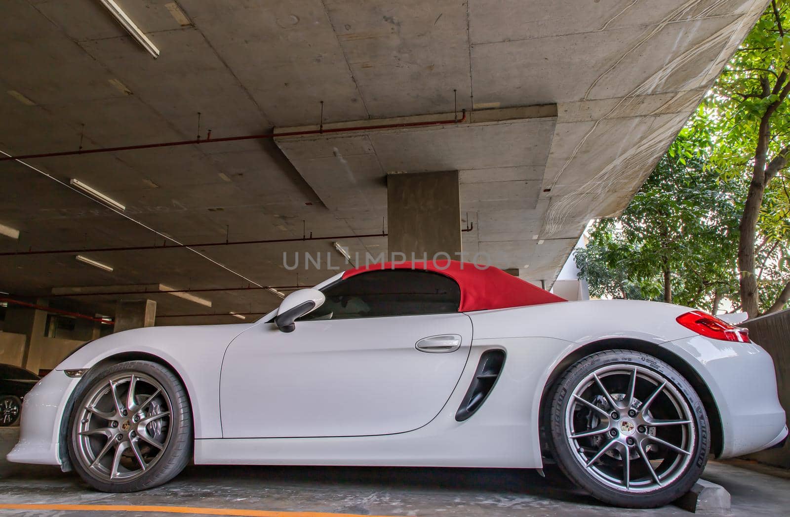 The side of Wheel of White Porsche Sports Car parked in the parking lot.  by tosirikul