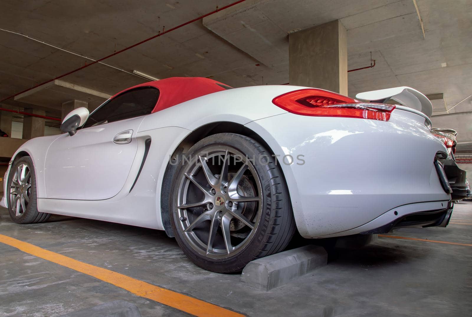 The side of Wheel of White Porsche Sports Car parked in the parking lot.  by tosirikul