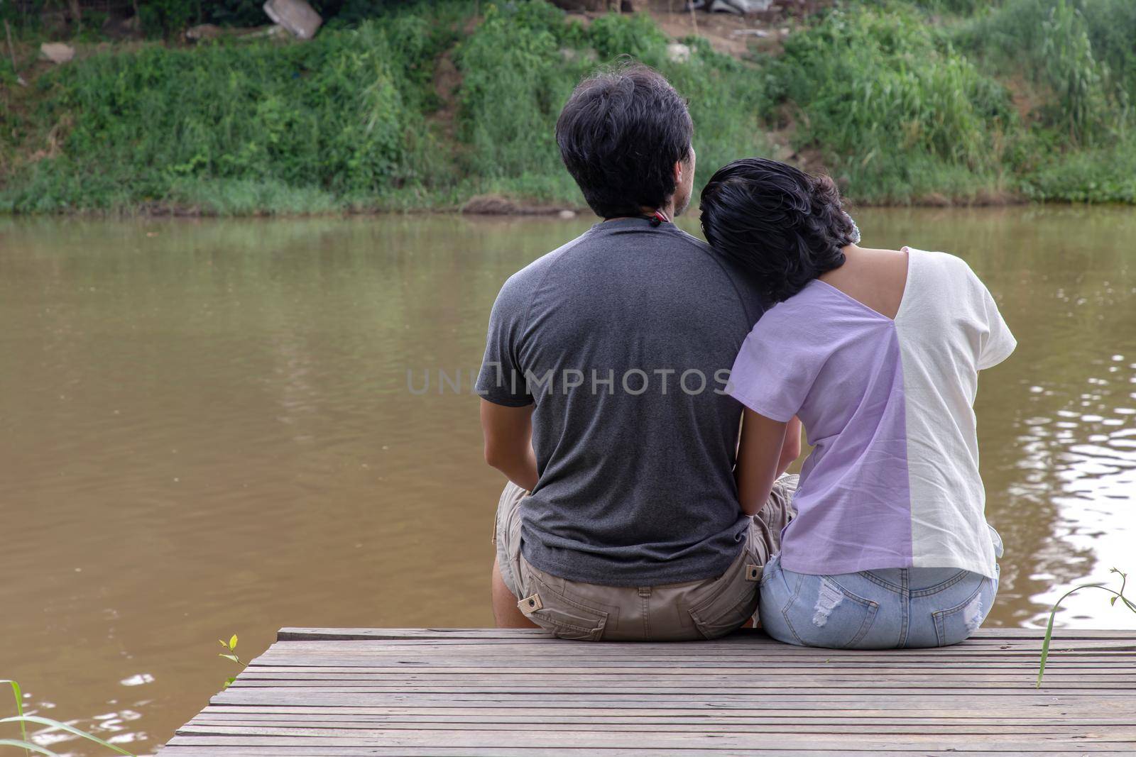 Rear view of young couple sitting in the border of a canal and watching river movement with together. Selective focus.