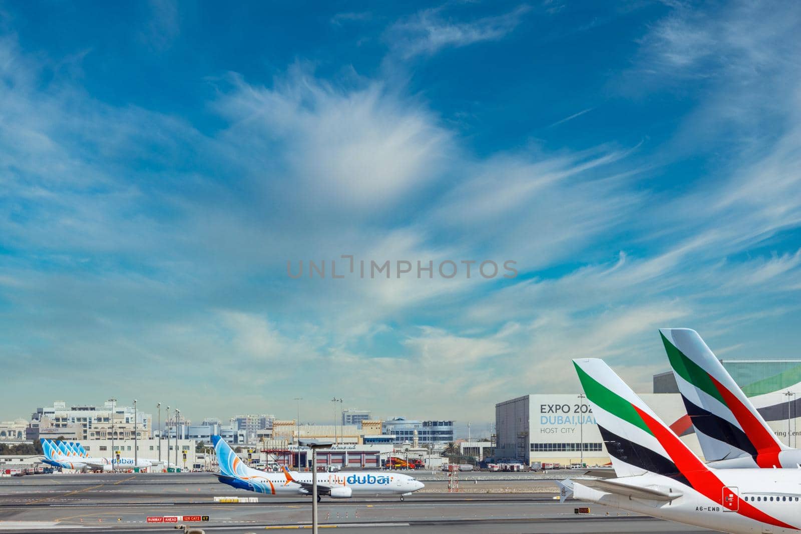 DUBAI, UAE - CIRCA 2021: DUBAI, UAE - CIRCA 2021: Emirates Airline and FlyDubai Airline Airplanes parked on Dubai Airport, on cloudy sky background.