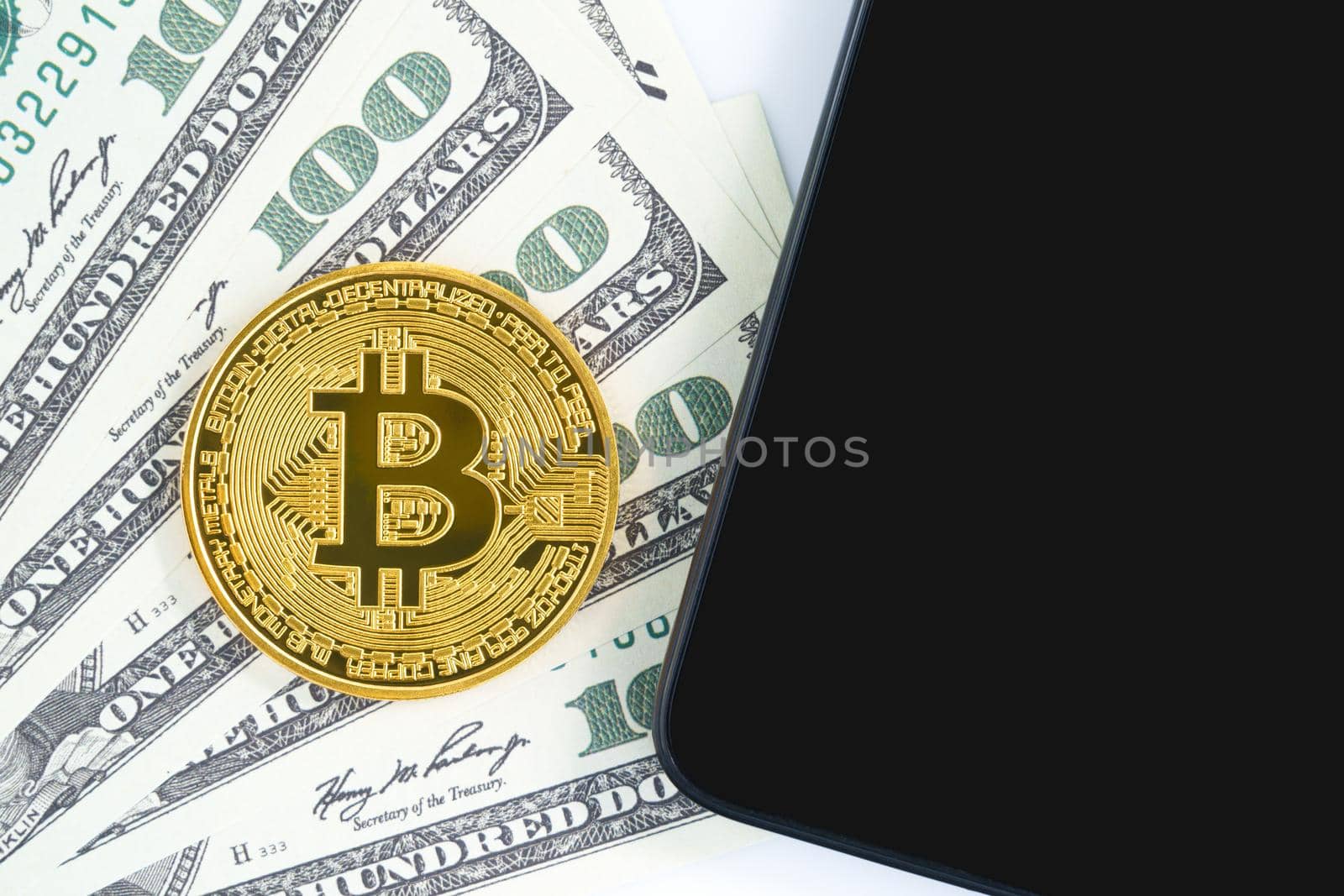 Bitcoins coin and  US banknotes of one hundred dollars with smartphone. Close up of metal shiny bitcoin crypto currency coins and US dollar