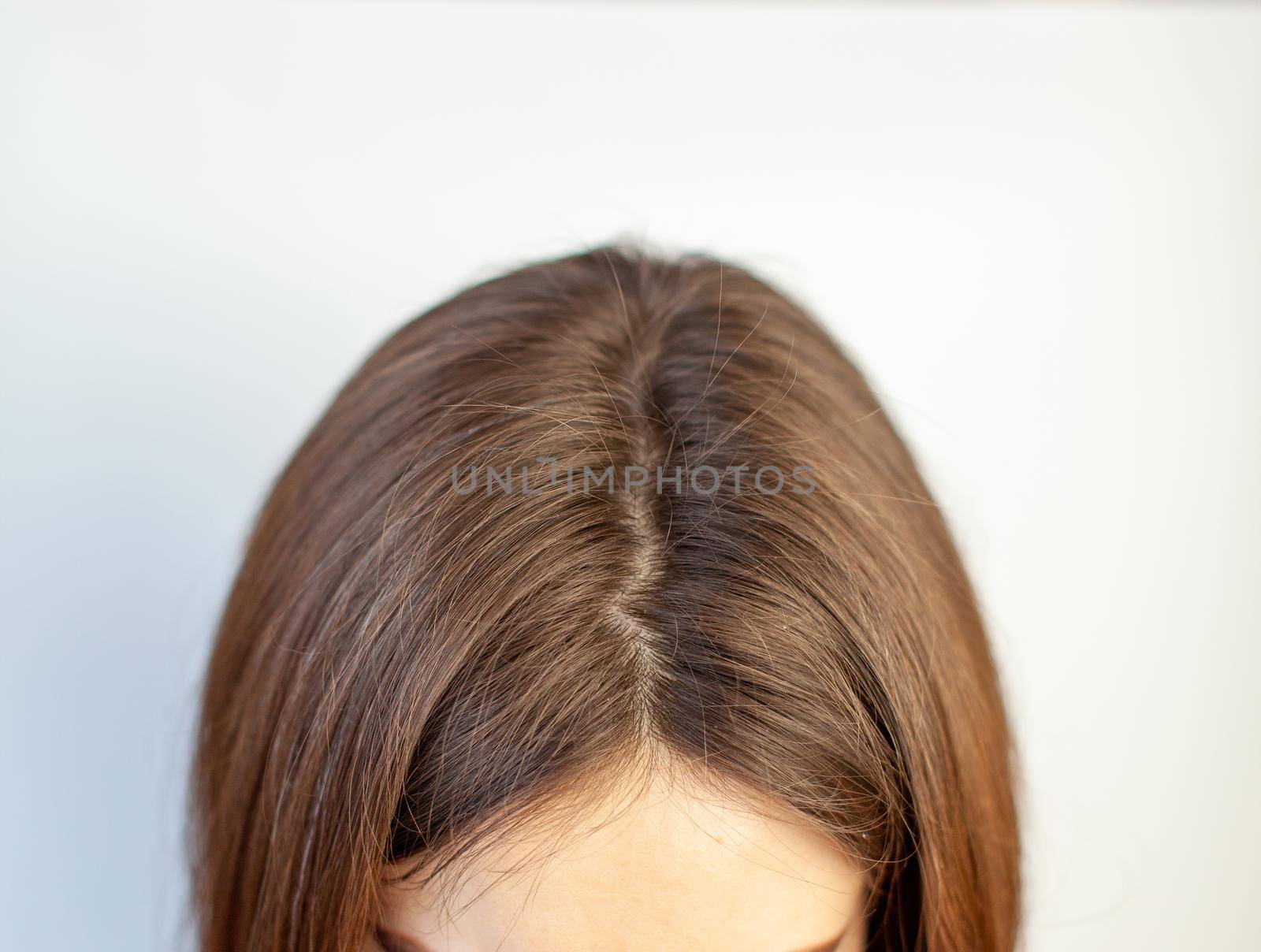 A woman's head with a parting of gray hair that has grown roots due to quarantine. Brown hair on a woman's head close-up.