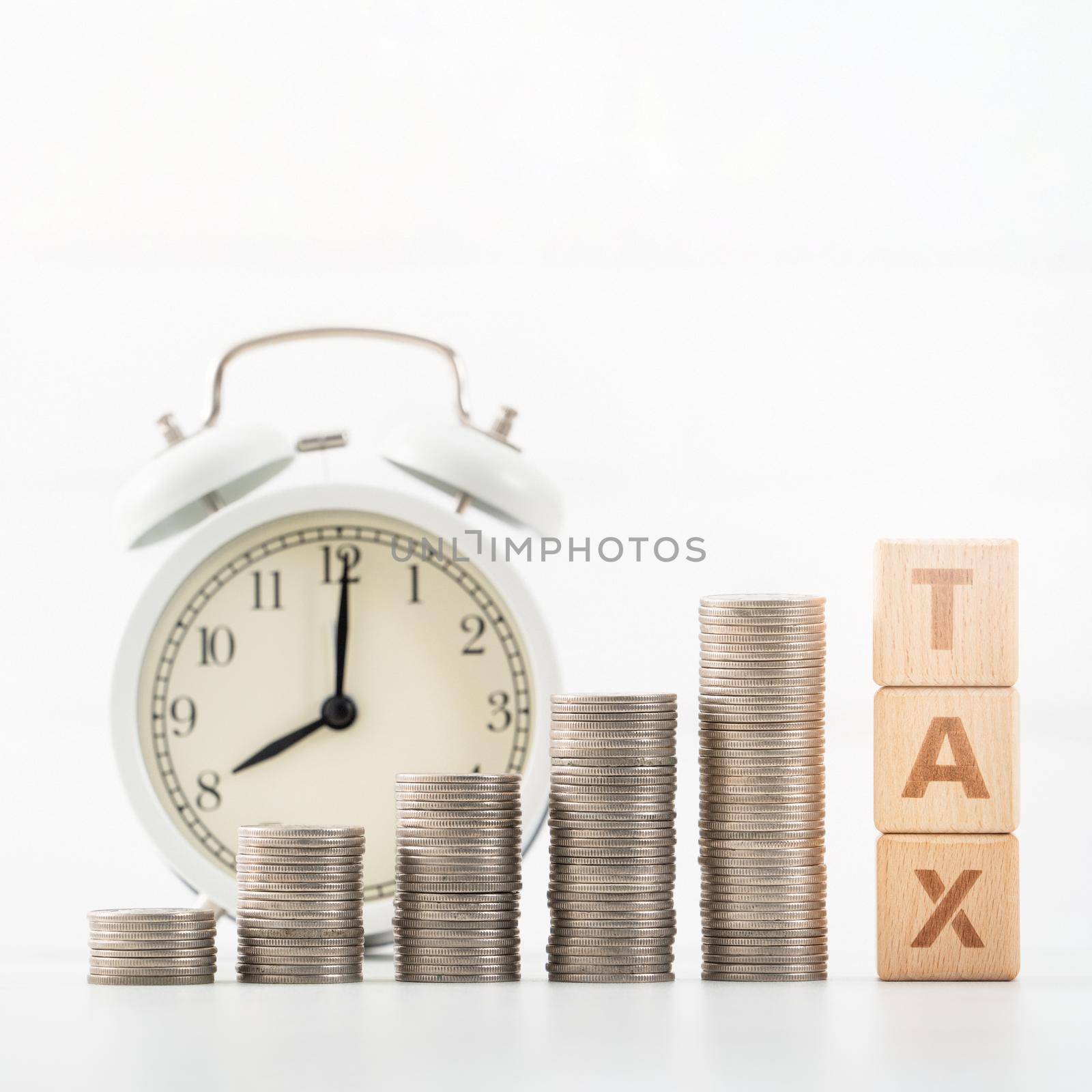 Concept of tax season approaching with wooden blocks, coins and alarm clock over white background.