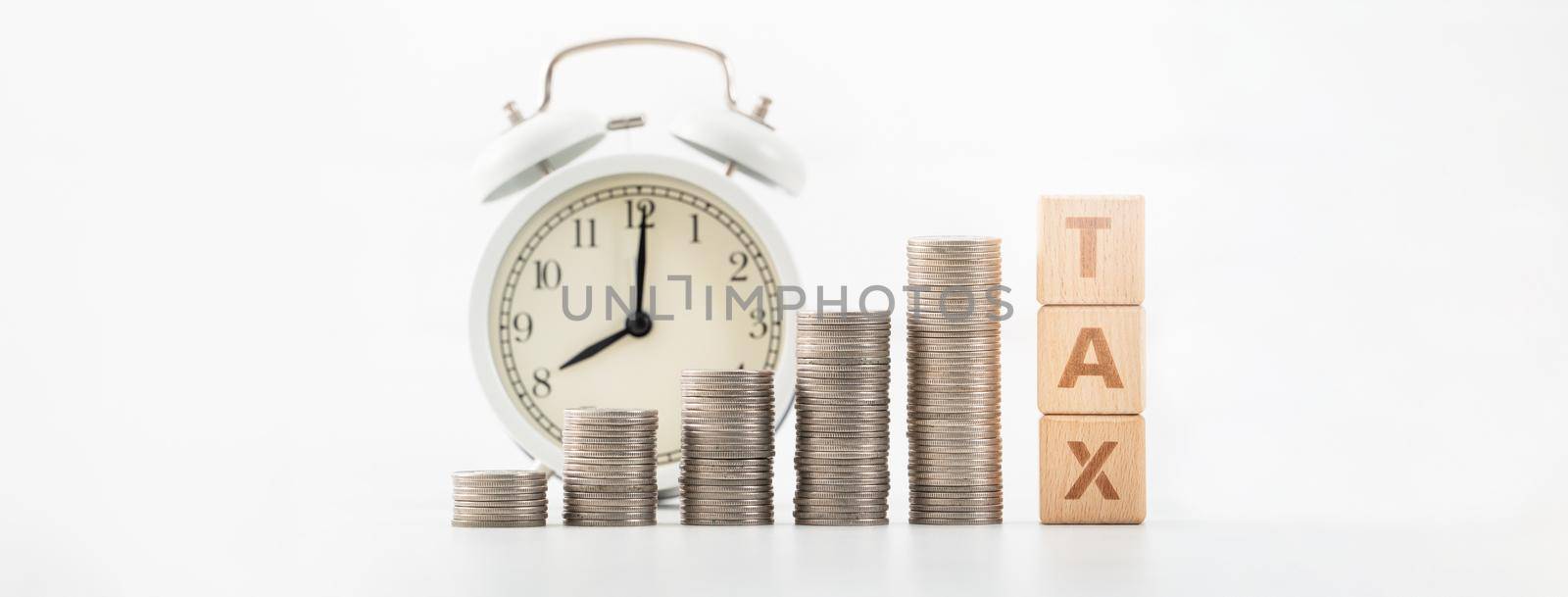 Concept of tax season approaching with wooden blocks, coins and alarm clock over white background.