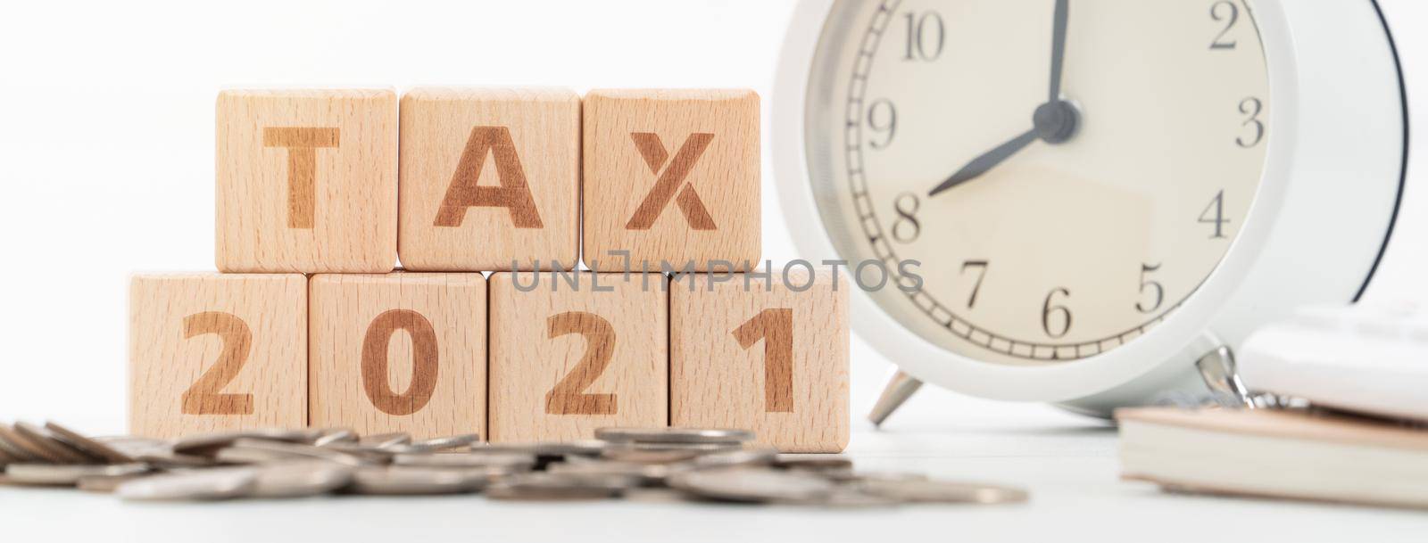 Concept of tax season approaching with wooden blocks, coins and alarm clock over white background.