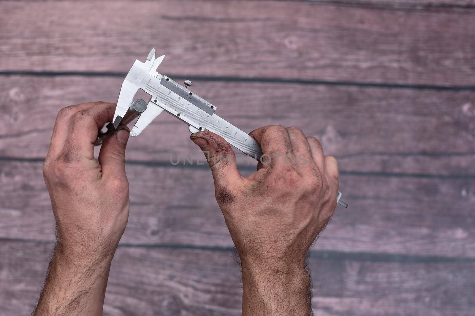 The worker measures the diameter of the drill with a caliper. His hands were dirty from his work. Close-up.