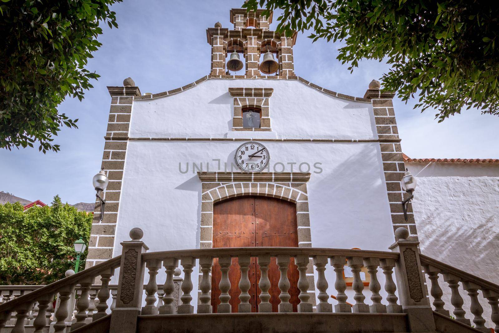 Low-angle view of the facade of a small church painted in white with a clock over the door