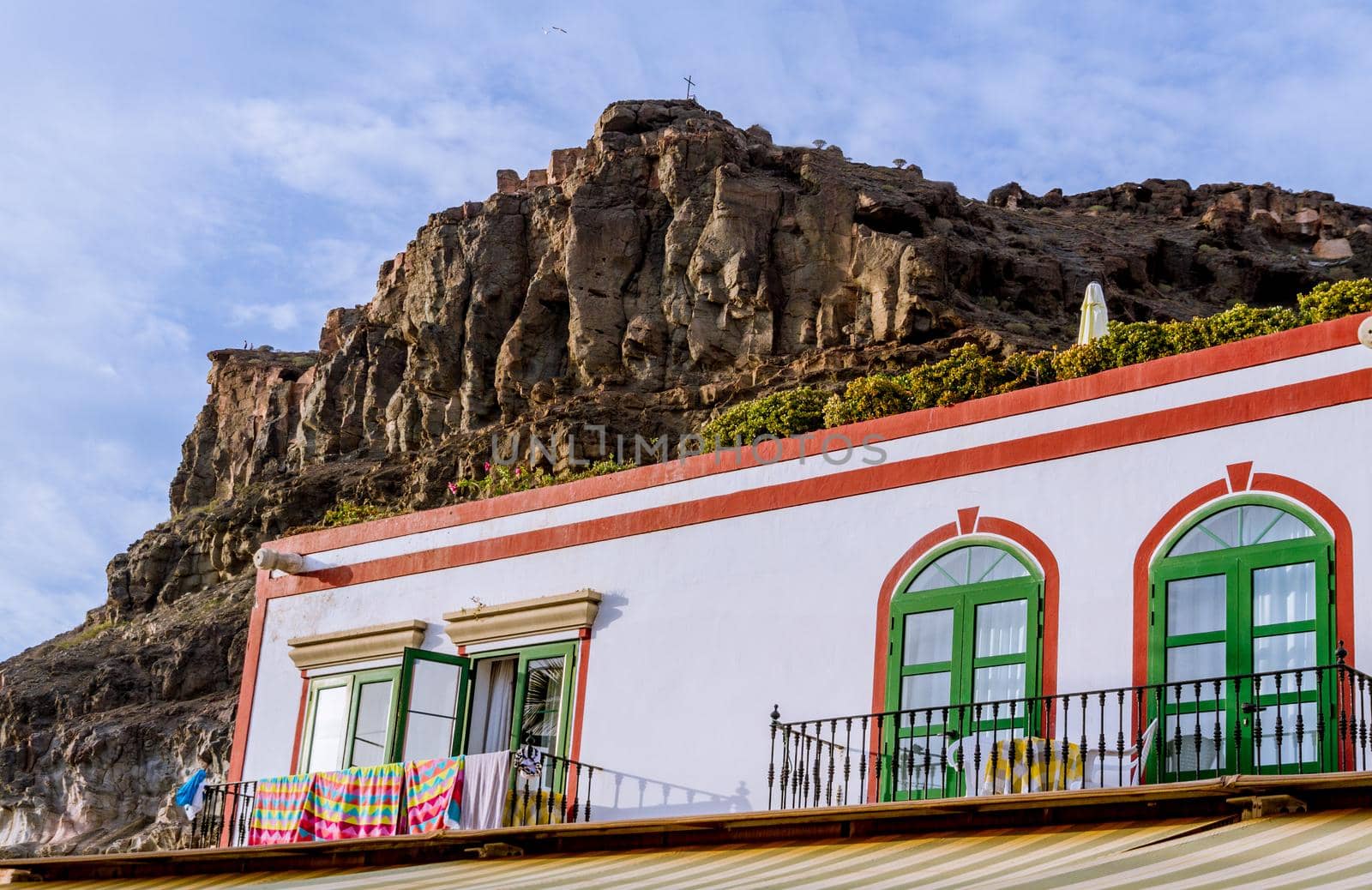 Detail of the facade of a house painted in white and red, with several windows and balconies and a rocky mountain in the background