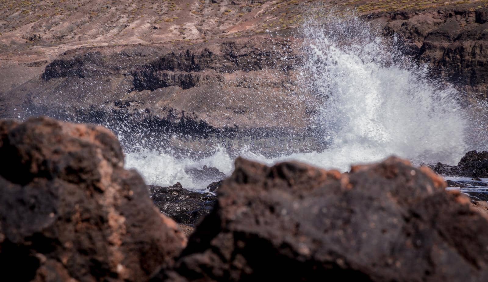 Big white waves clashing against the coast with black volcanic rocks in the foreground