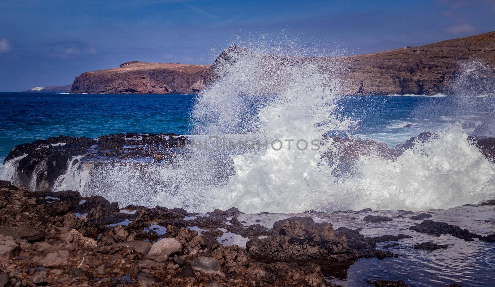 Wide shot of a rocky beach with waves breaking on the rocks on a sunny day