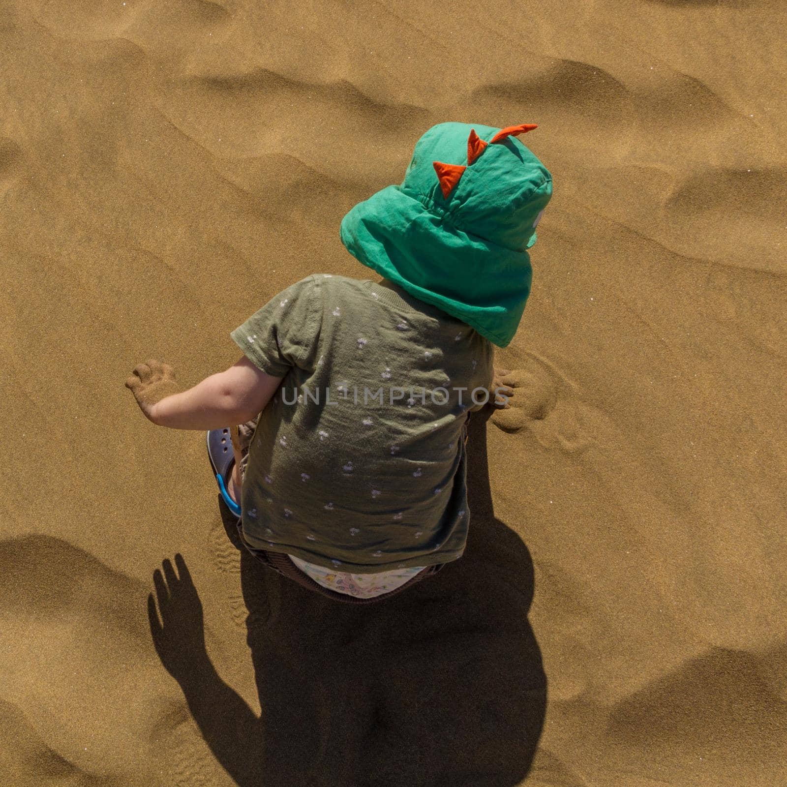 High-angle view of a baby boy wearing a green hat playing with the sand on the beach