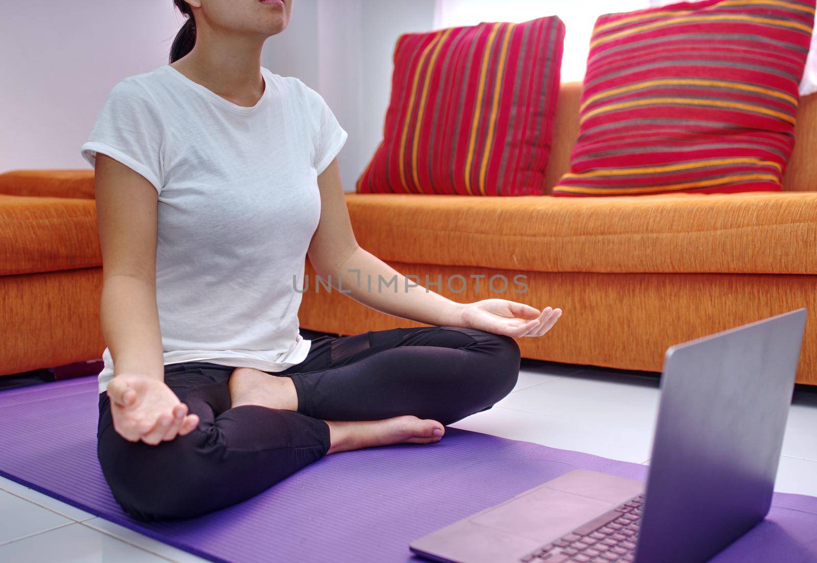 A young woman doing exercise as a model from an online course on her laptop by noppha80