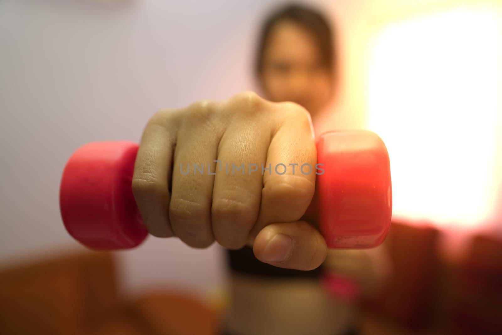 Asian woman training to lift pink dumbbells for building muscle, concept of staying healthy by weight loss and recreation at their own residence.