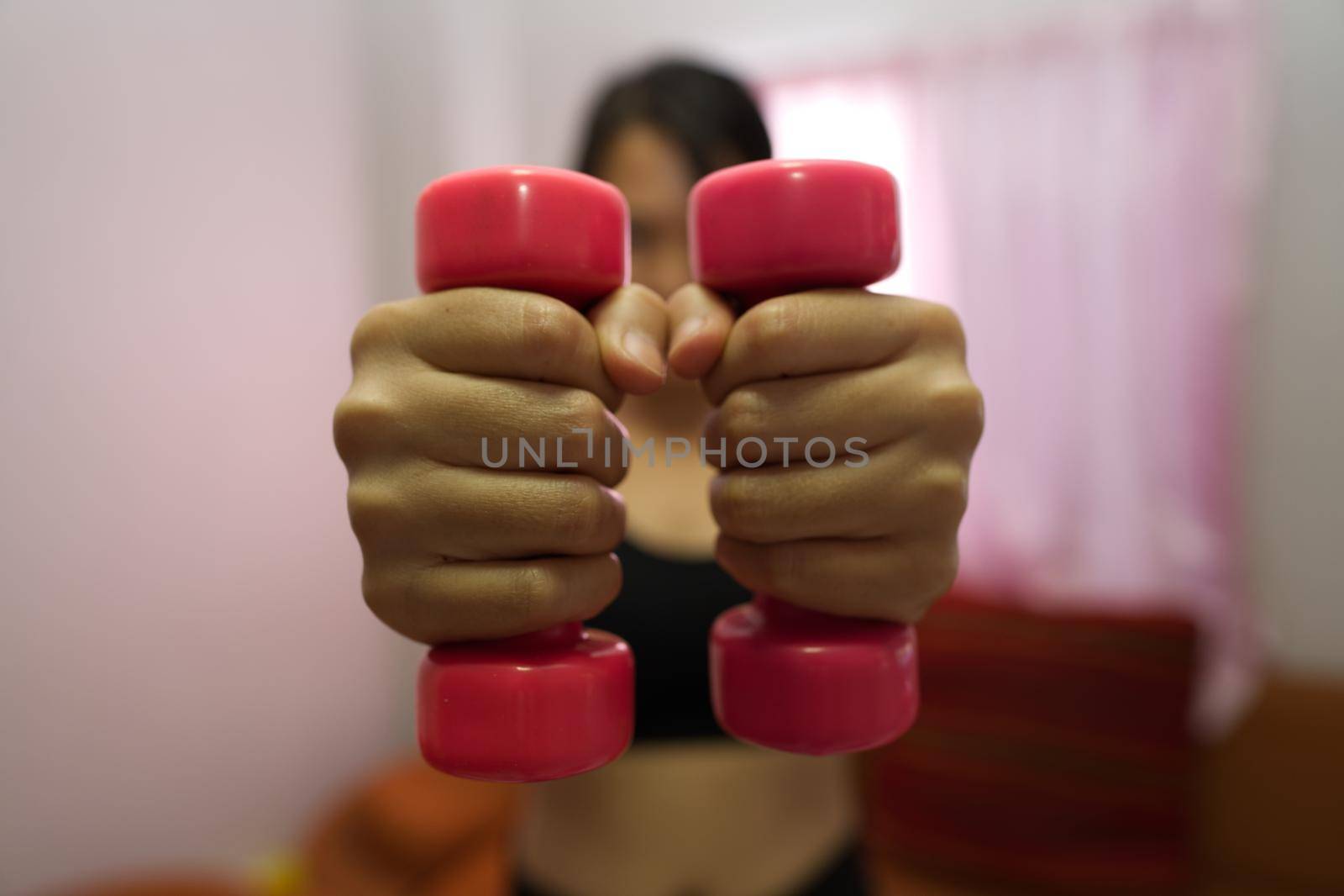 Asian woman training to lift pink dumbbells for building muscle, concept of staying healthy by weight loss and recreation at their own residence. by noppha80