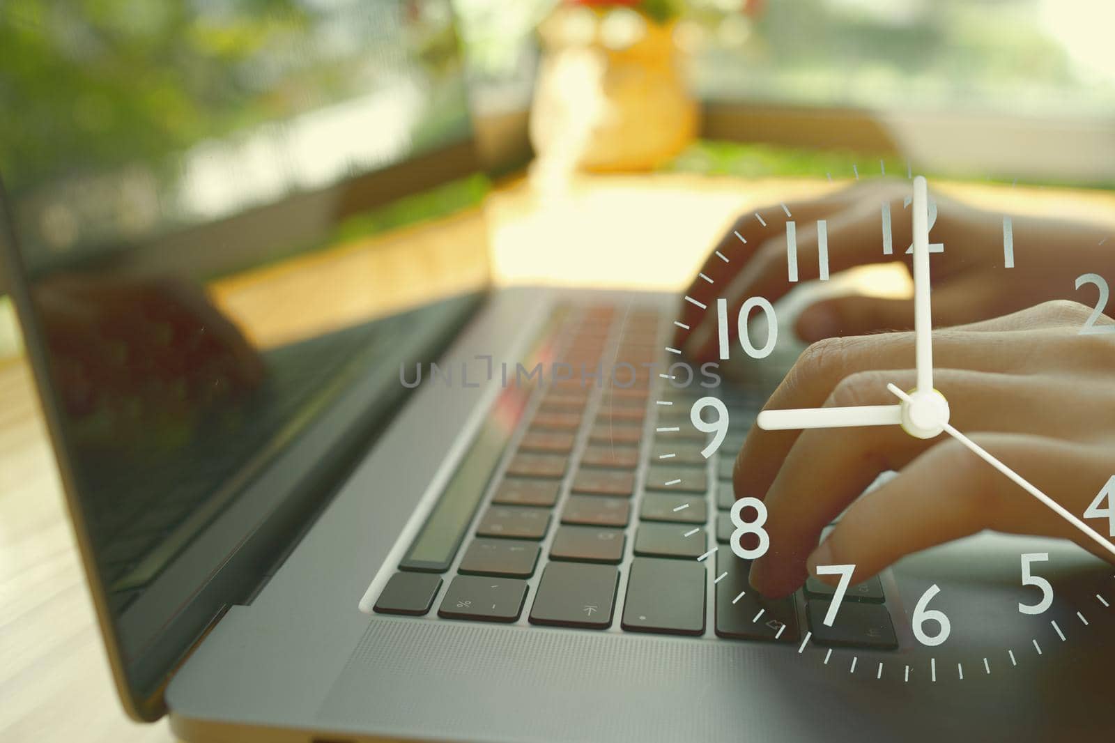 An abstract hand typing a laptop and an analog clock showing the start time of the workplace.