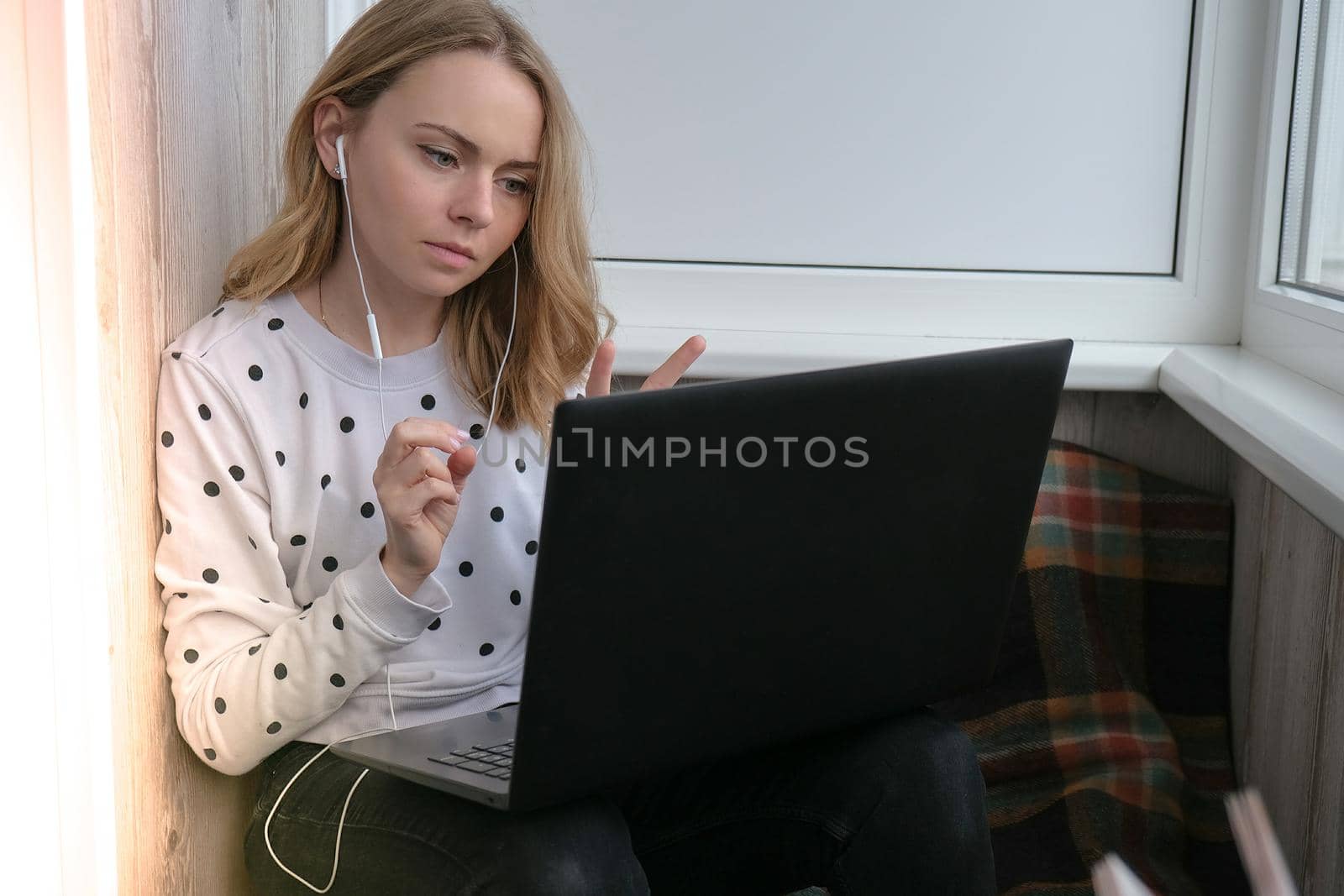 Young woman sitting on balcony next to laptop. Online education. Stay home concept. Work from home. Earphones