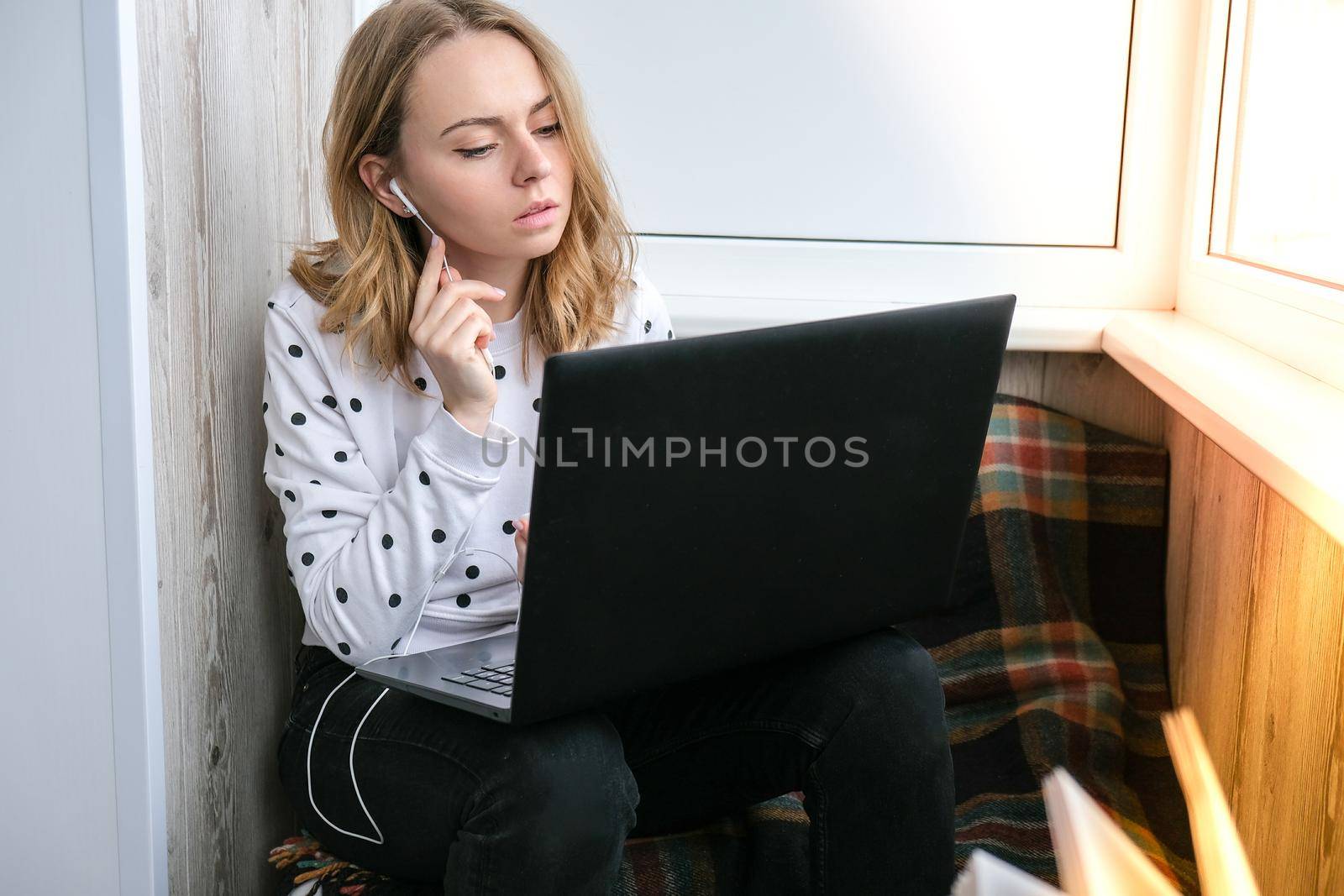 Young woman sitting on balcony next to laptop. Online education. Stay home concept. Work from home. Earphones