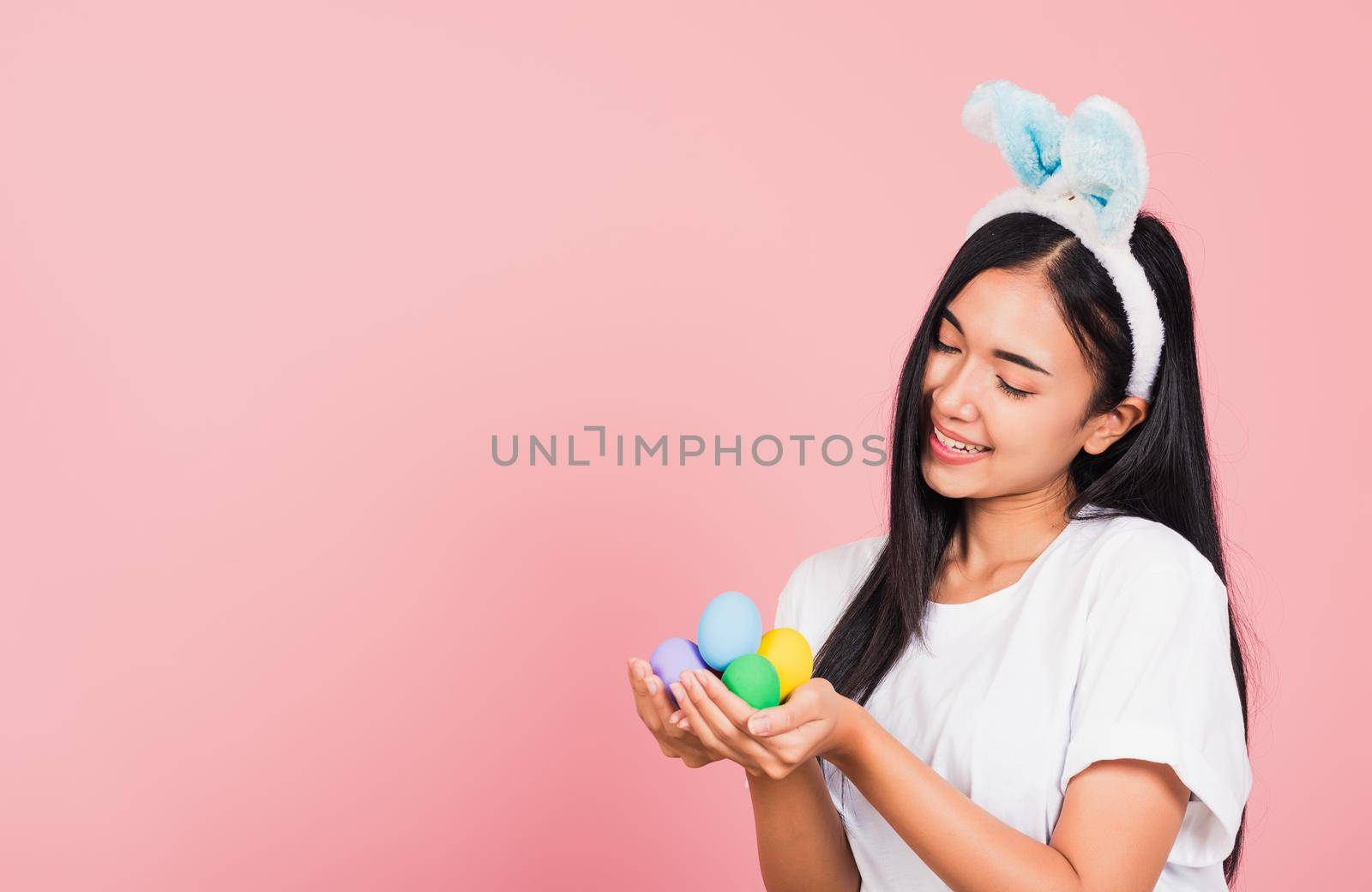 woman smiling wearing rabbit ears holding colorful Easter eggs gift on hands by Sorapop
