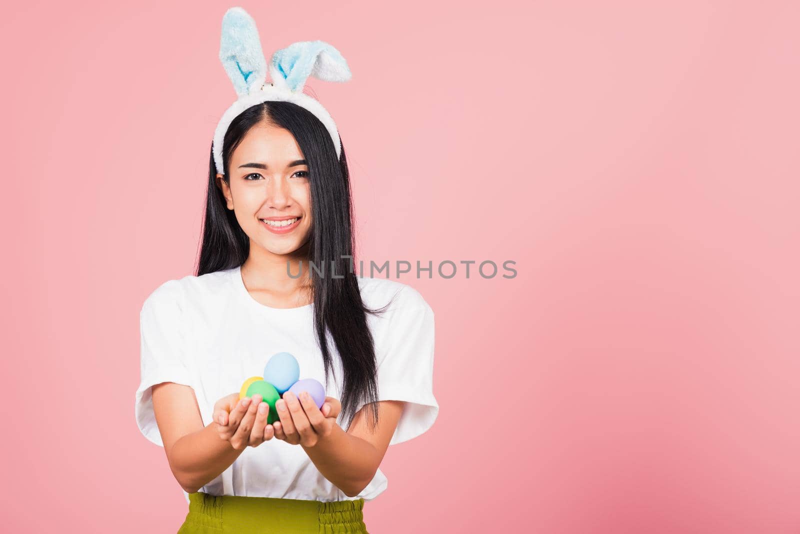 Happy Easter concept. Beautiful young woman smiling wearing rabbit ears holding colorful Easter eggs gift on hands, Portrait female looking at camera, studio shot isolated on pink background