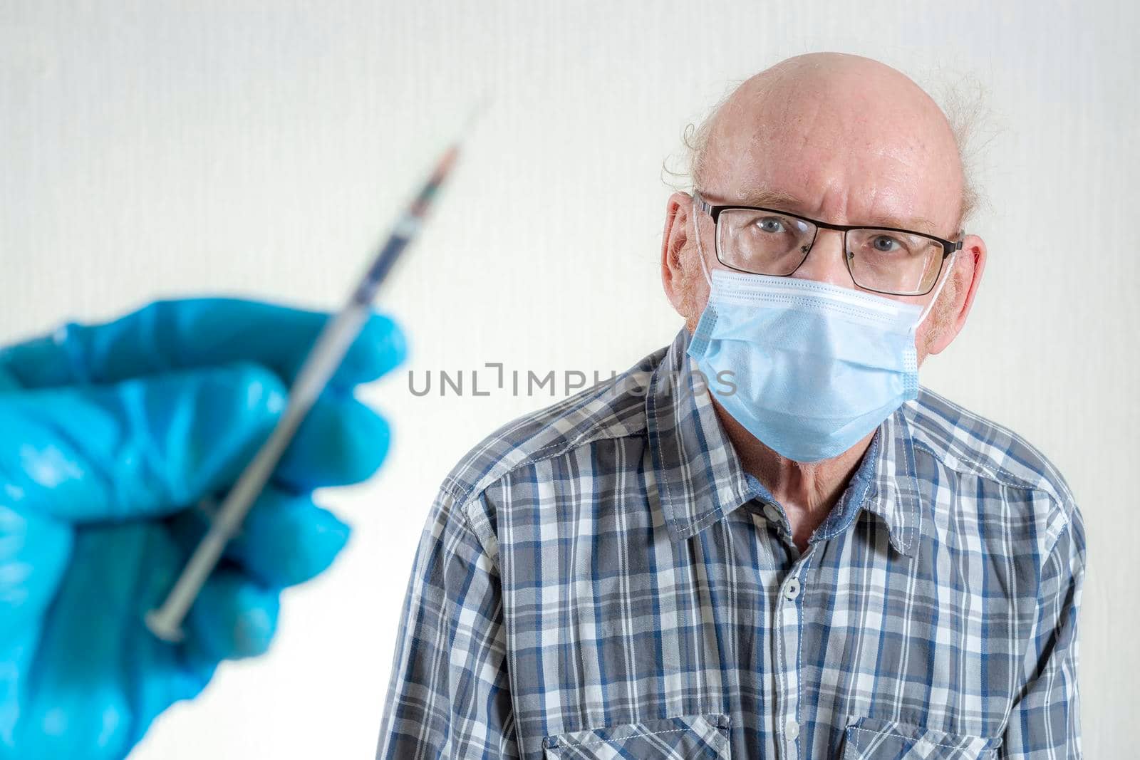 A syringe in his hand with a vaccine and a patient is an old man. Indoors in daylight. Front view. by Essffes