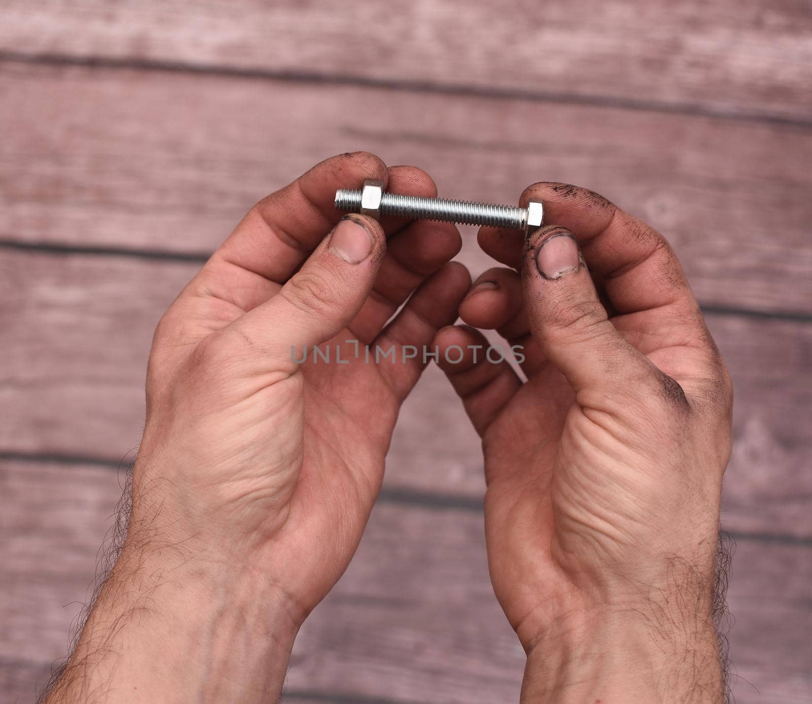 The man is holding a bolt with a screwed nut. Close-up on a wooden background. Dirty hands from work.