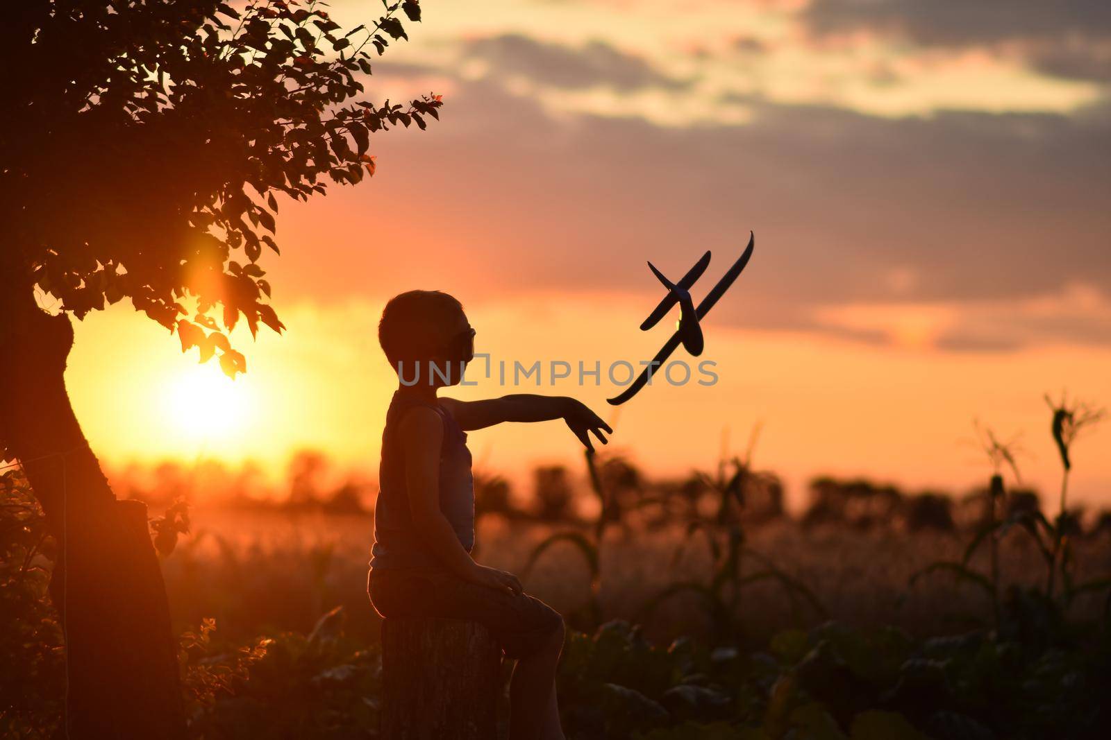 The boy launches the plane into flight at sunset. The child wants to become an aviator pilot. The concept of playing on the street without gadgets. 