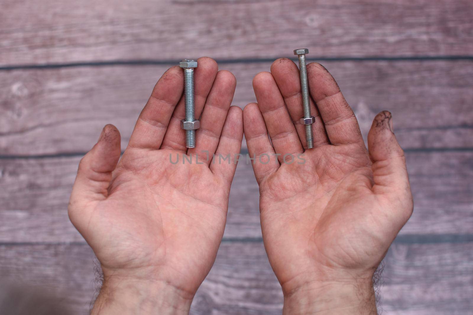two bolts and nuts in working men's hands. On a wooden background.