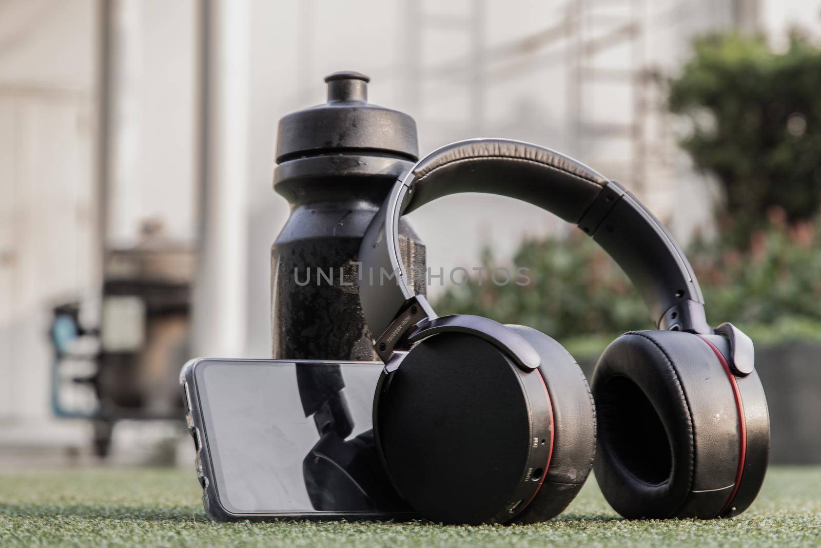 Composition of Smartphone and Headphones for listening to music and water bottle Placed on green grass In the time of rest, Summer lawn with personal device with Space for text.