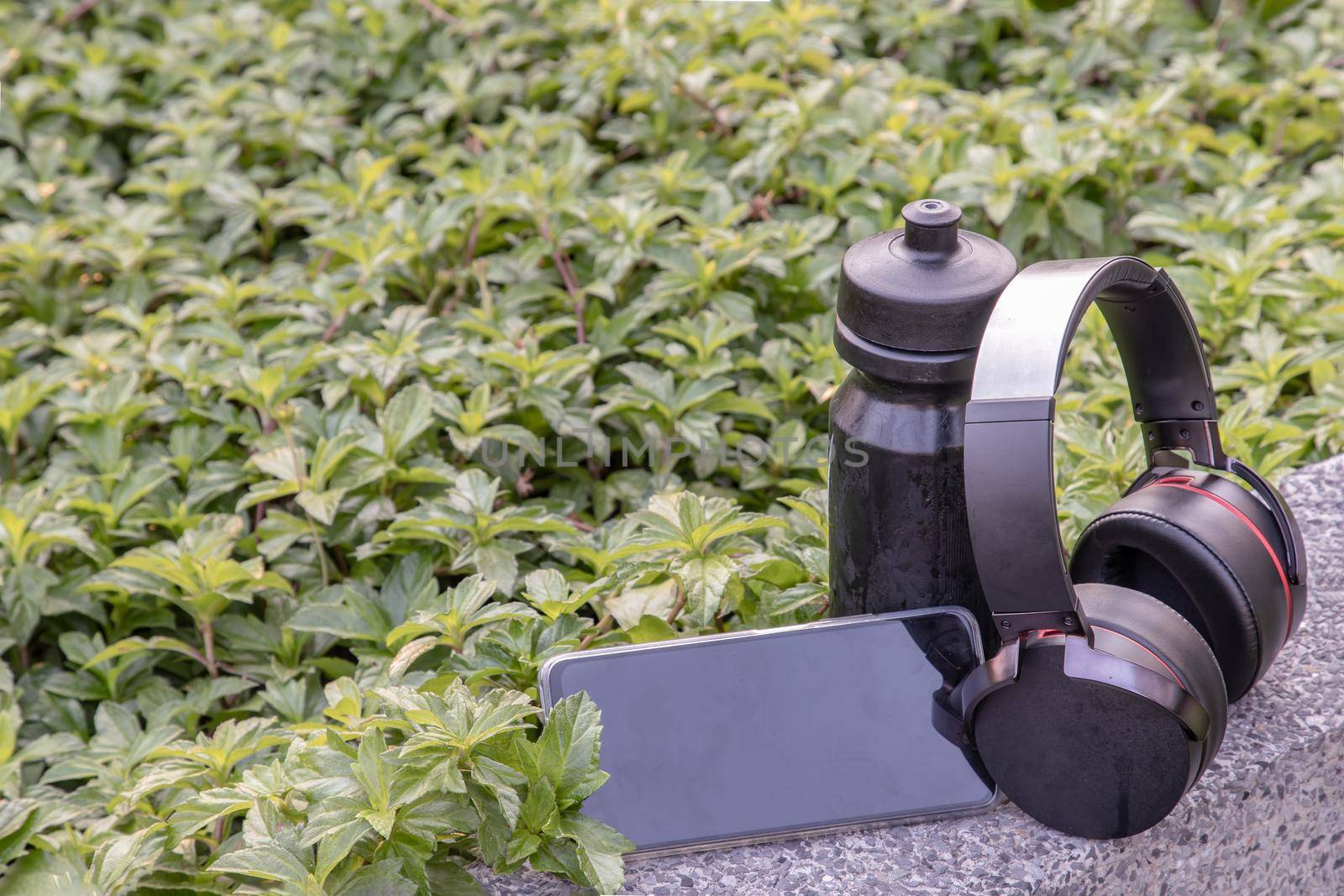Composition of Smartphone and Headphones for listening to music and water bottle Placed on natural green background In the time of rest. Personal device with Space for text, Selective focus.