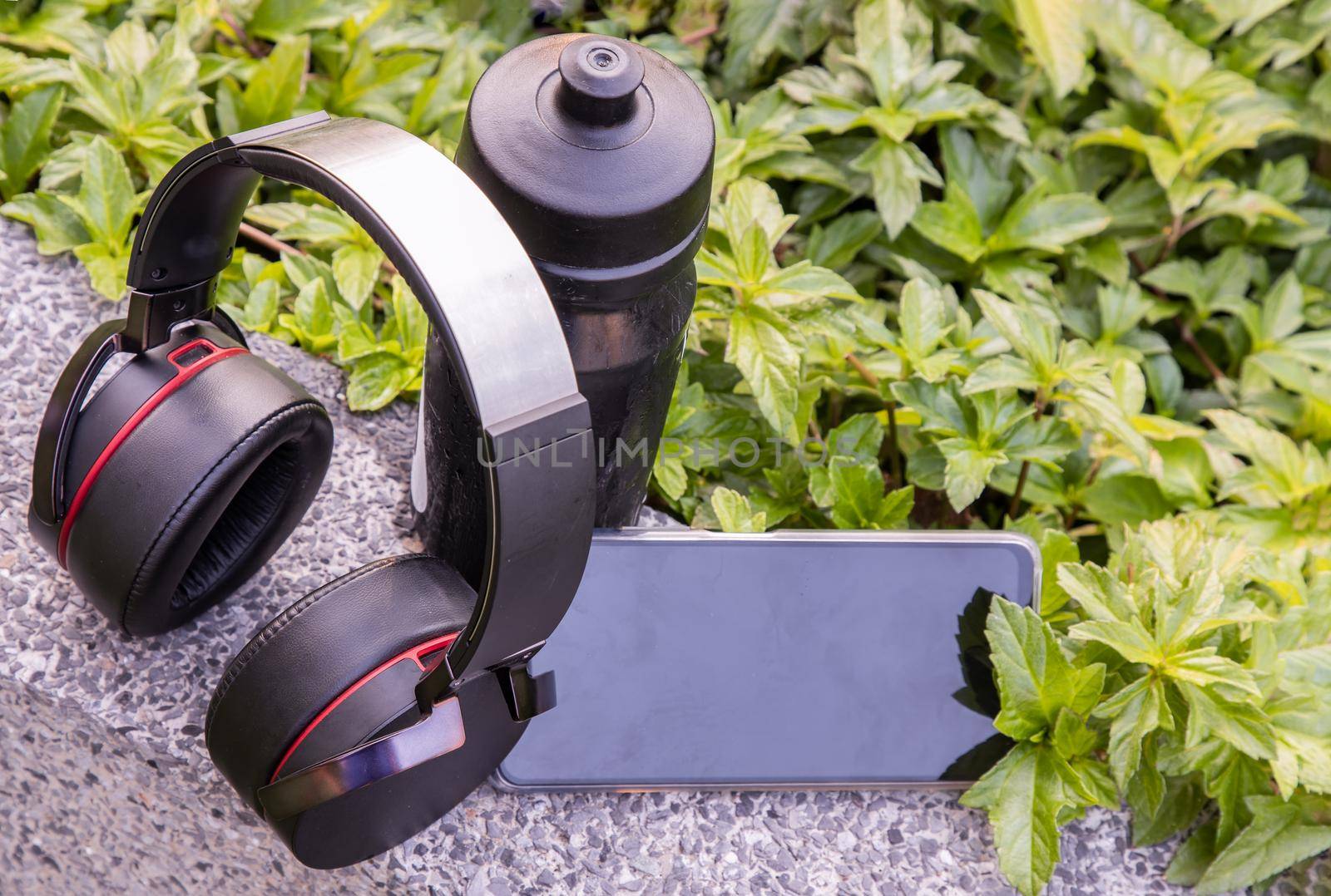 Composition of Smartphone and Headphones for listening to music and water bottle Placed on natural green background In the time of rest. Personal device with Space for text, Selective focus.