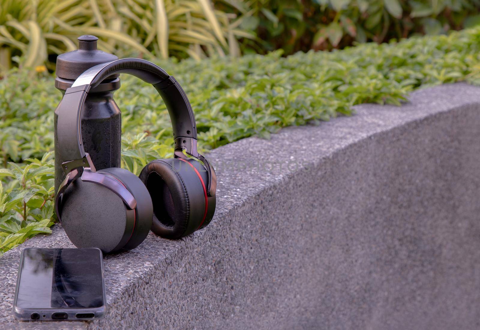 Composition of Smartphone and Headphones for listening to music and water bottle Placed on natural green background In the time of rest. Personal device with Space for text, Selective focus.