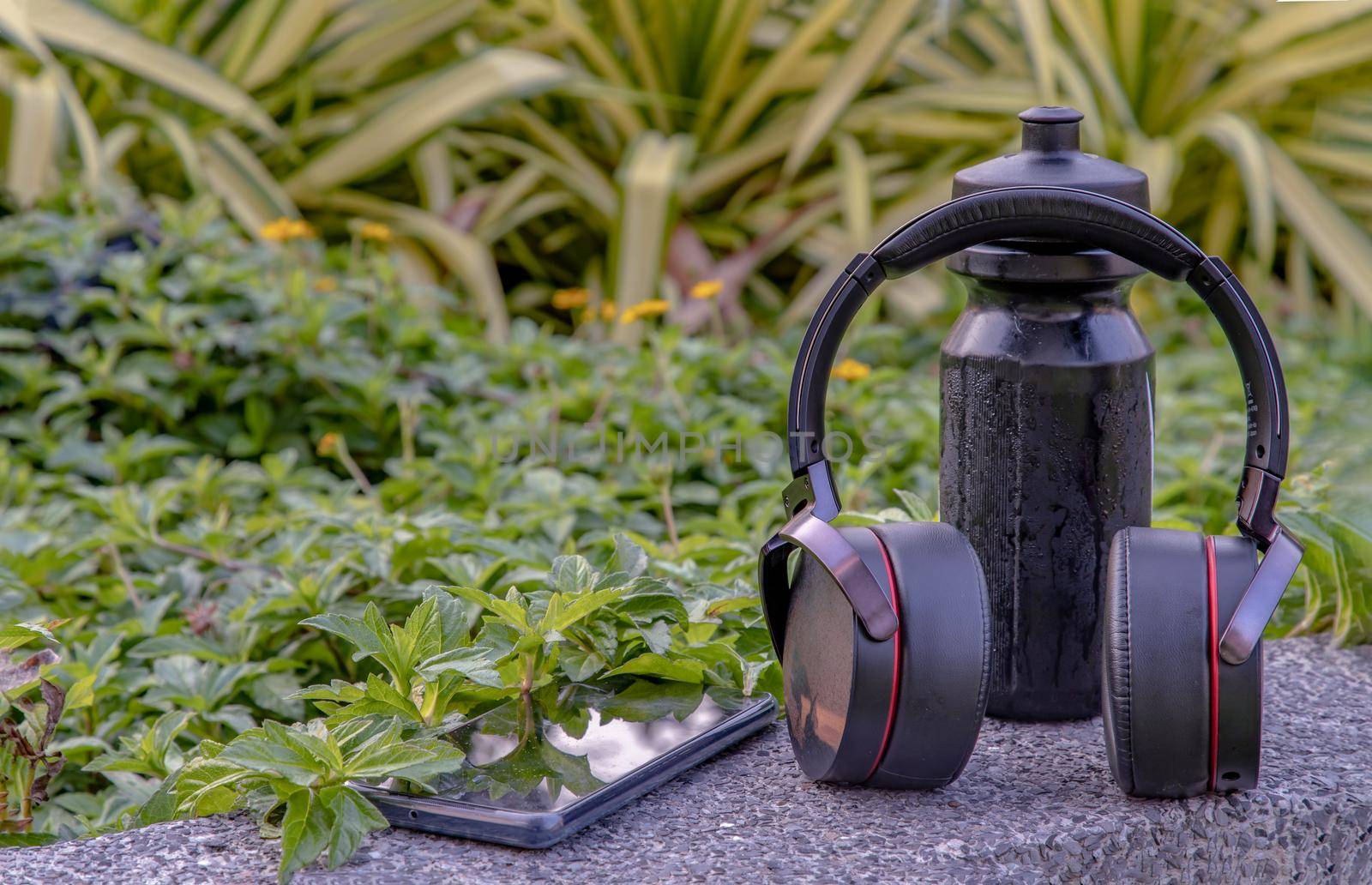 Composition of Smartphone and Headphones for listening to music and water bottle Placed on natural green background In the time of rest. Personal device with Space for text, Selective focus.