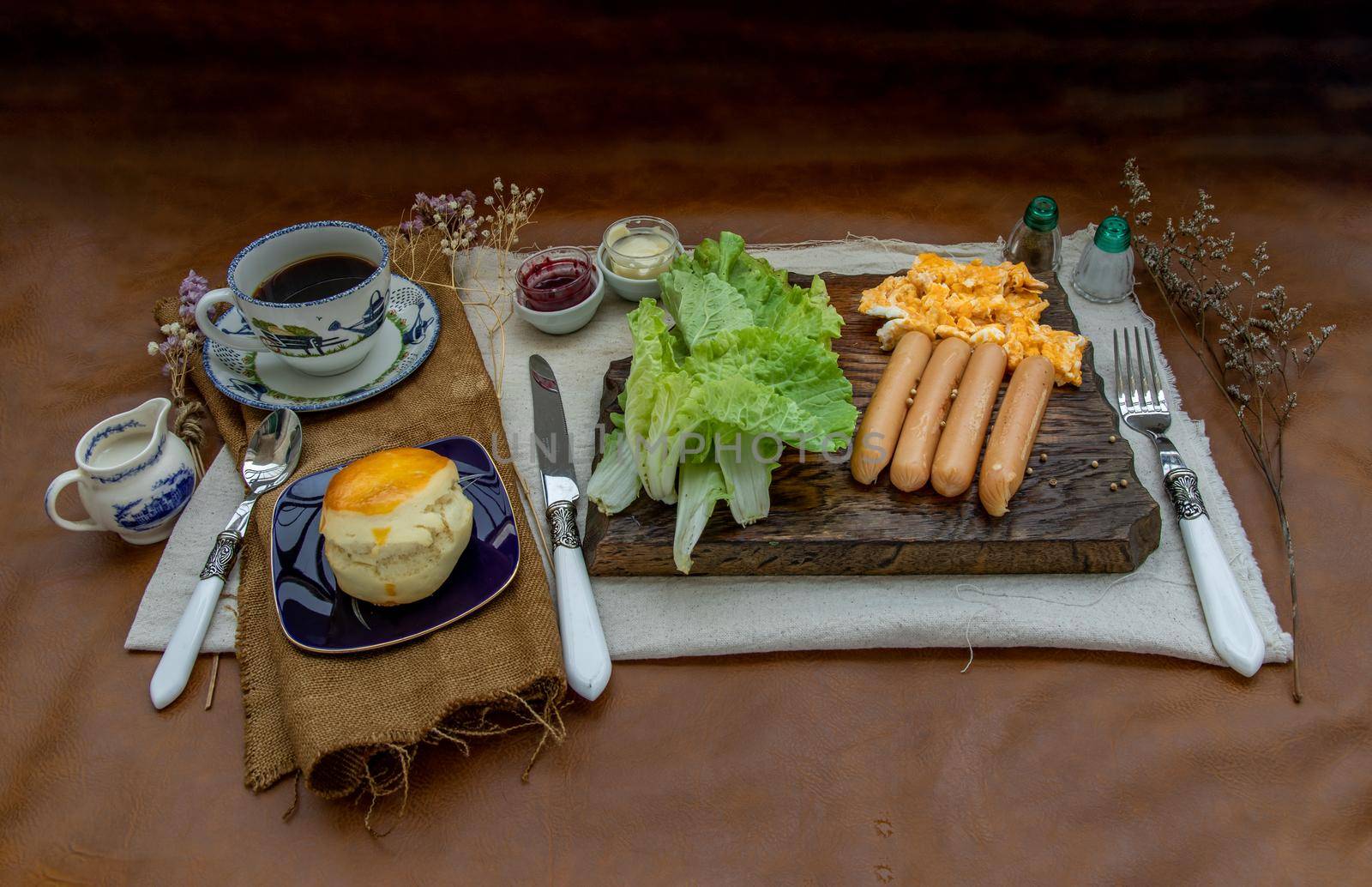 Continental breakfast with scrambled eggs, fried sausages, vegetable and scones served with coffee with milk. Wood background, Selective focuse.