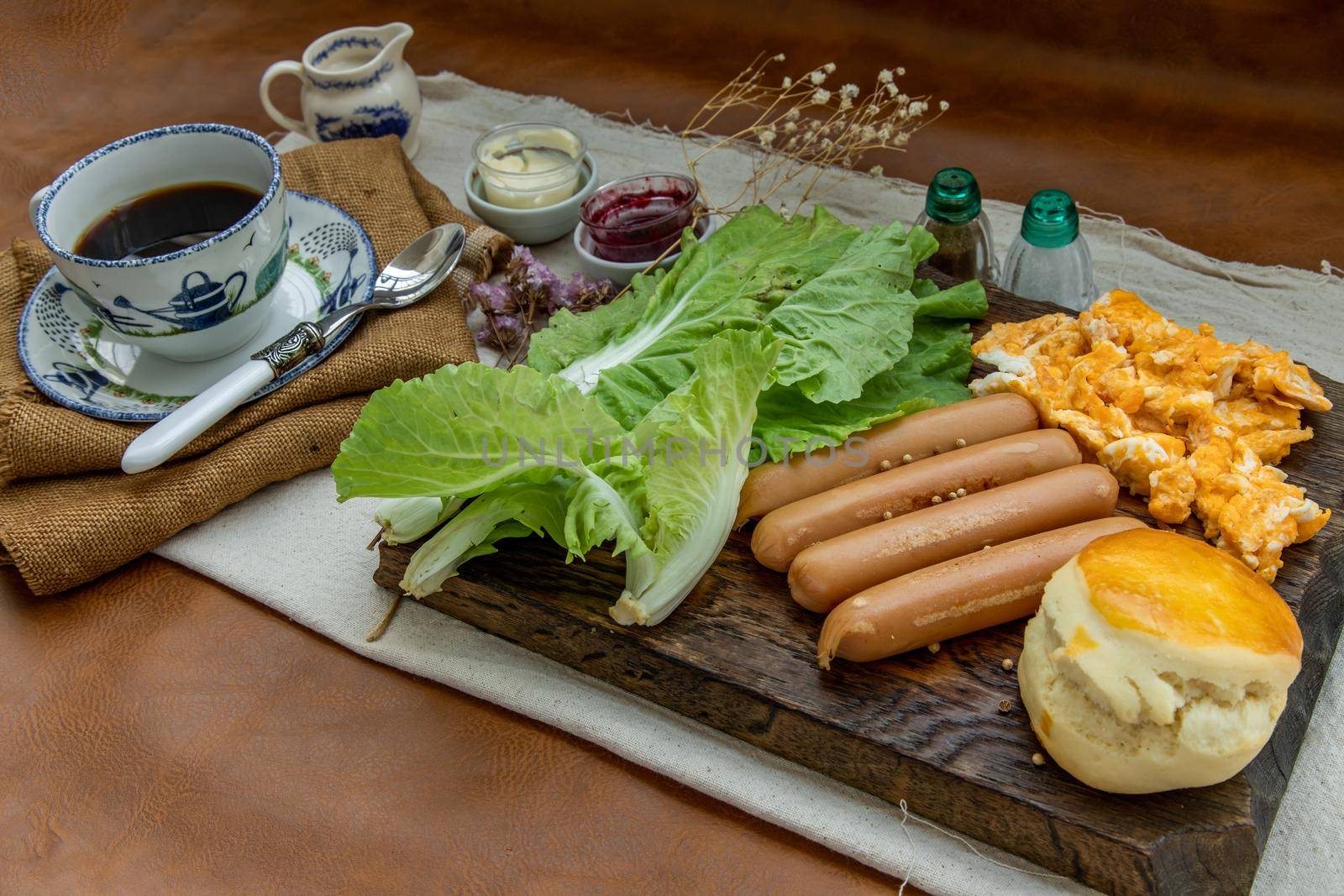 Continental breakfast with scrambled eggs, fried sausages, vegetable and scones served with coffee with milk. Wood background, Selective focuse.